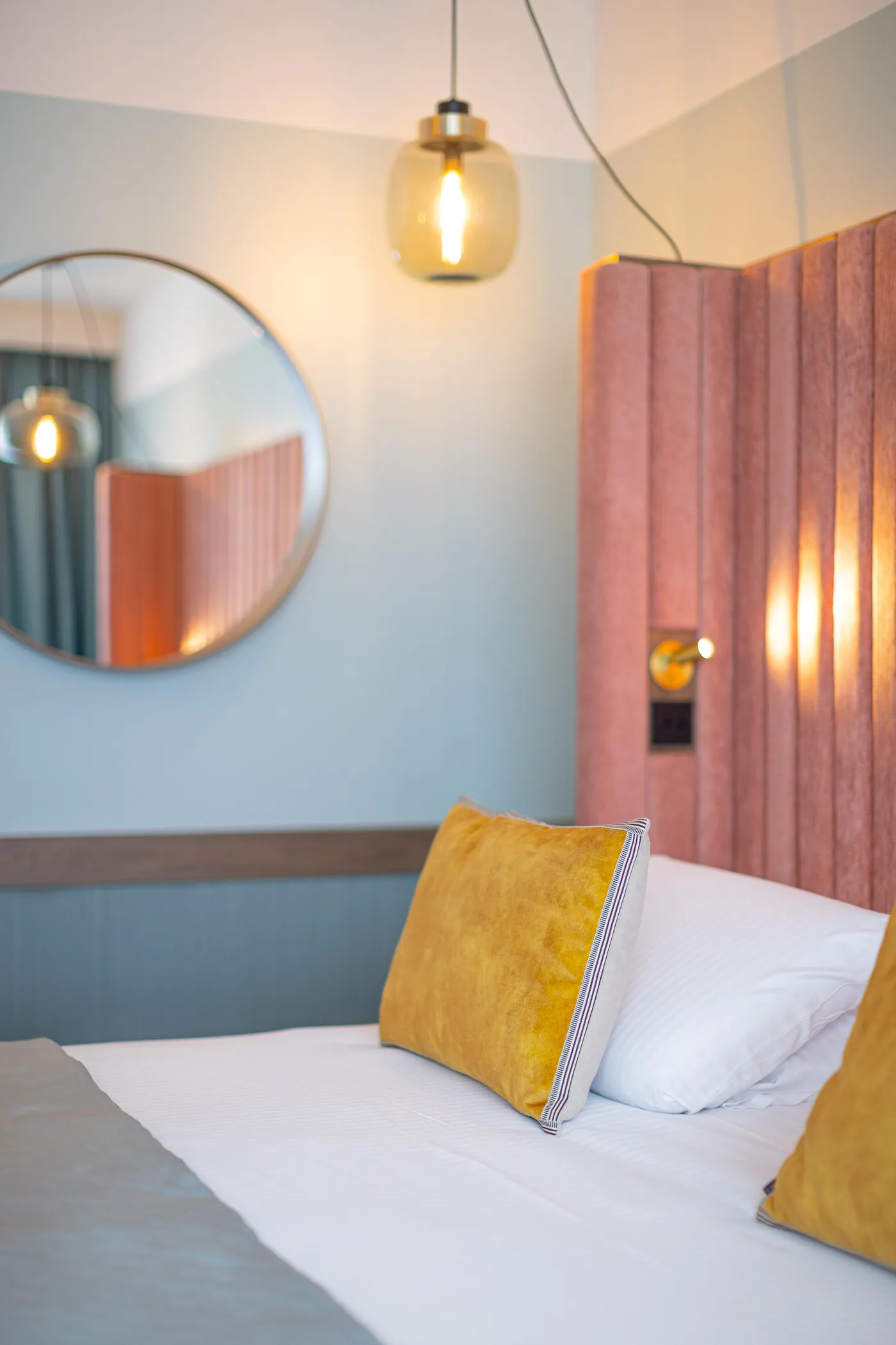 Lit avec des coussins jaunes, une lampe suspendue et un miroir rond sur le mur