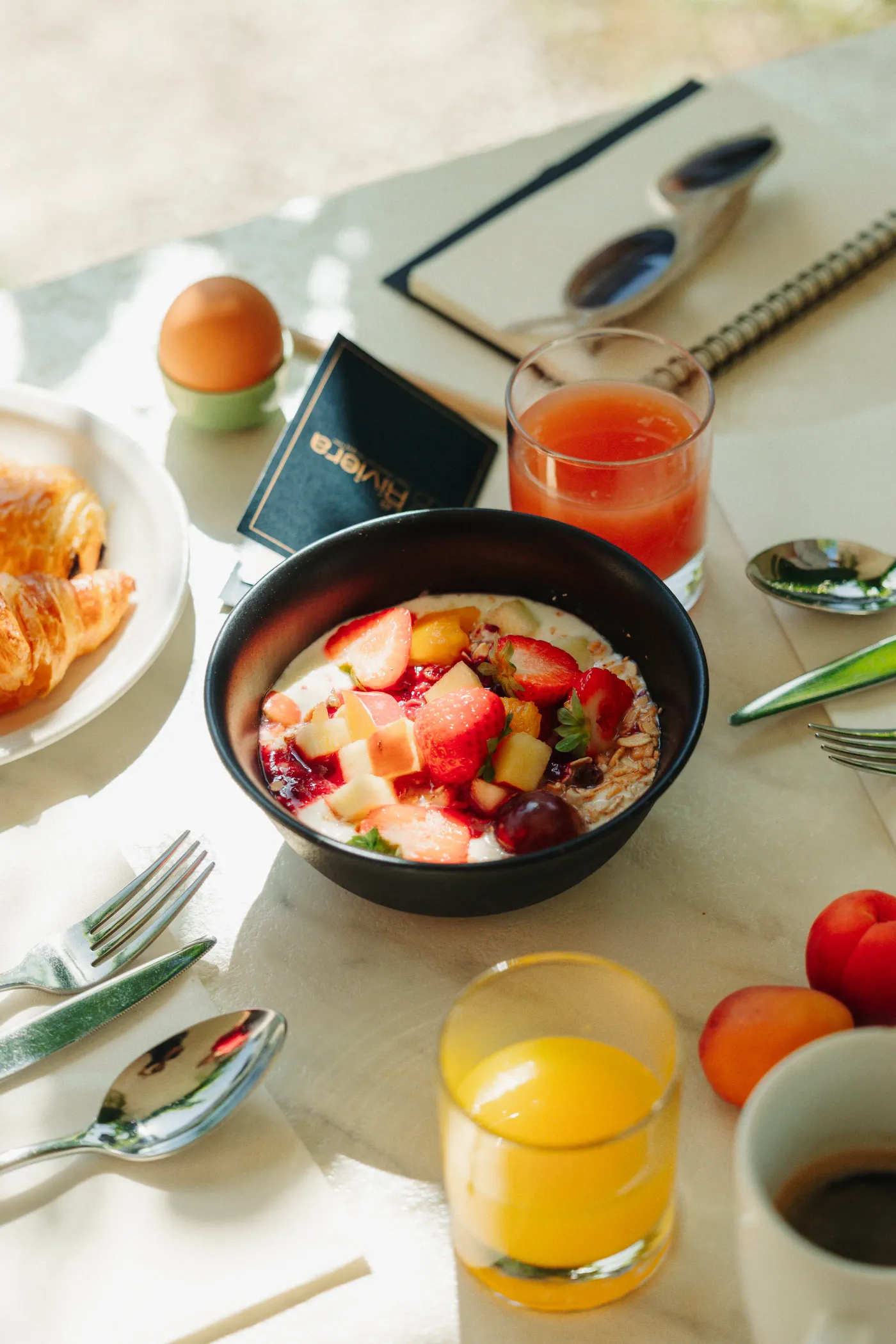 A bowl of fruit porridge, croissants, glasses of juice, cutlery, and eggs on a table