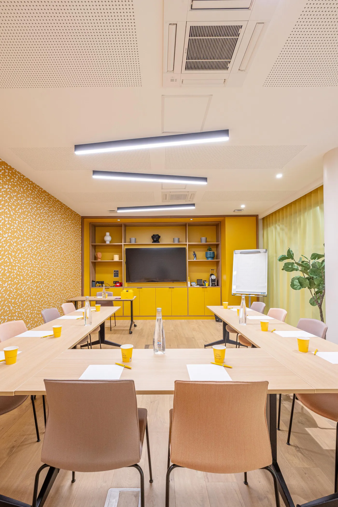 Salle de réunion avec tables, chaises, écran, tableau blanc et décoration murale jaune