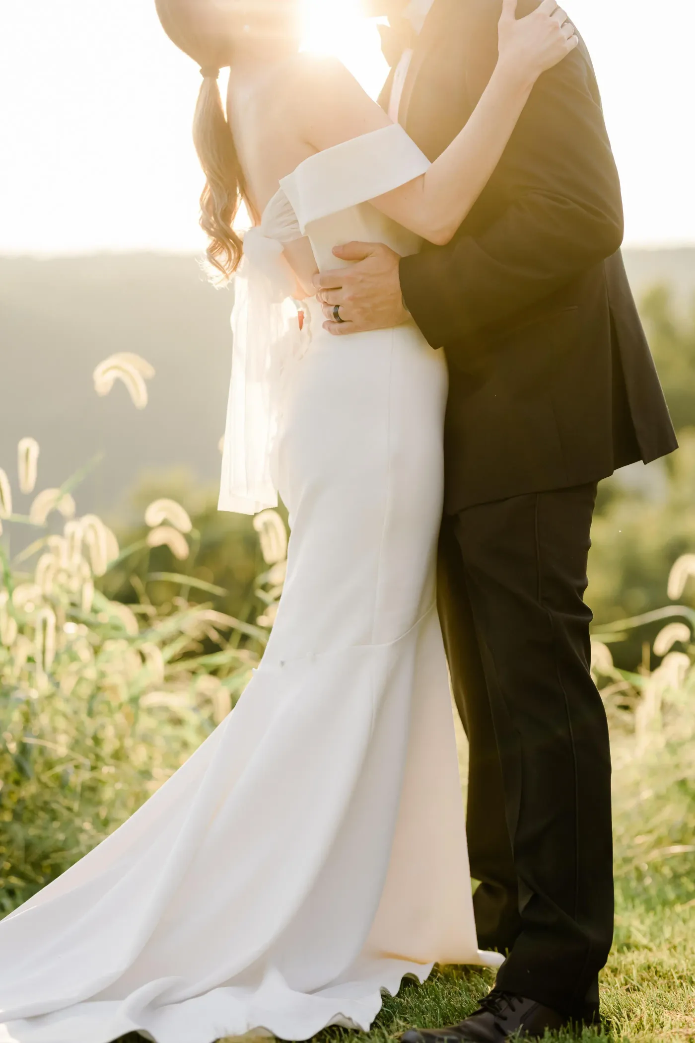Un couple en tenue de mariage s'embrasse dans un champ avec des plantes en arrière-plan
