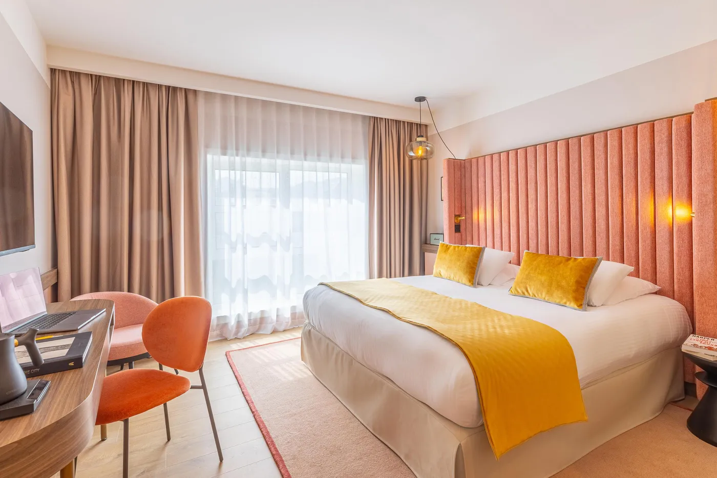 Chambre d'hôtel avec un lit double, des rideaux, une table de travail, deux chaises et une grande fenêtre