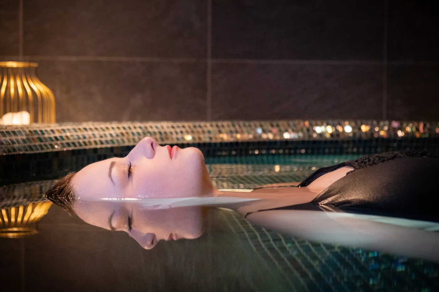 A person lying on their back in a pool with a blurred night view in the background