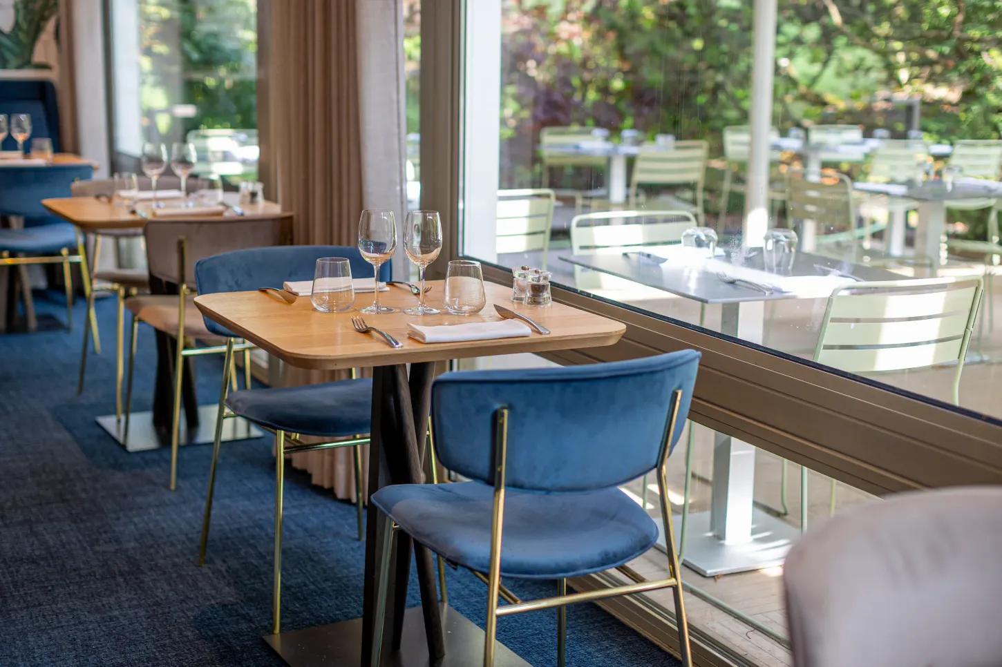 Table dressée avec verres et couverts dans un restaurant aux grandes baies vitrées donnant sur un jardin