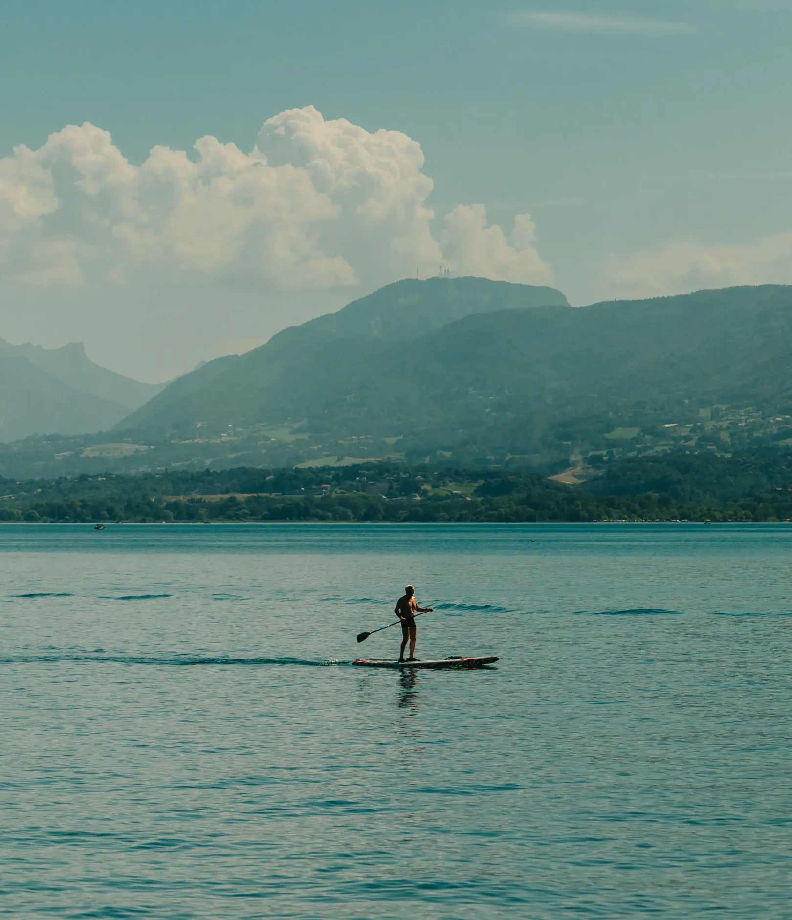A person is paddleboarding on a lake with mountains in the background.