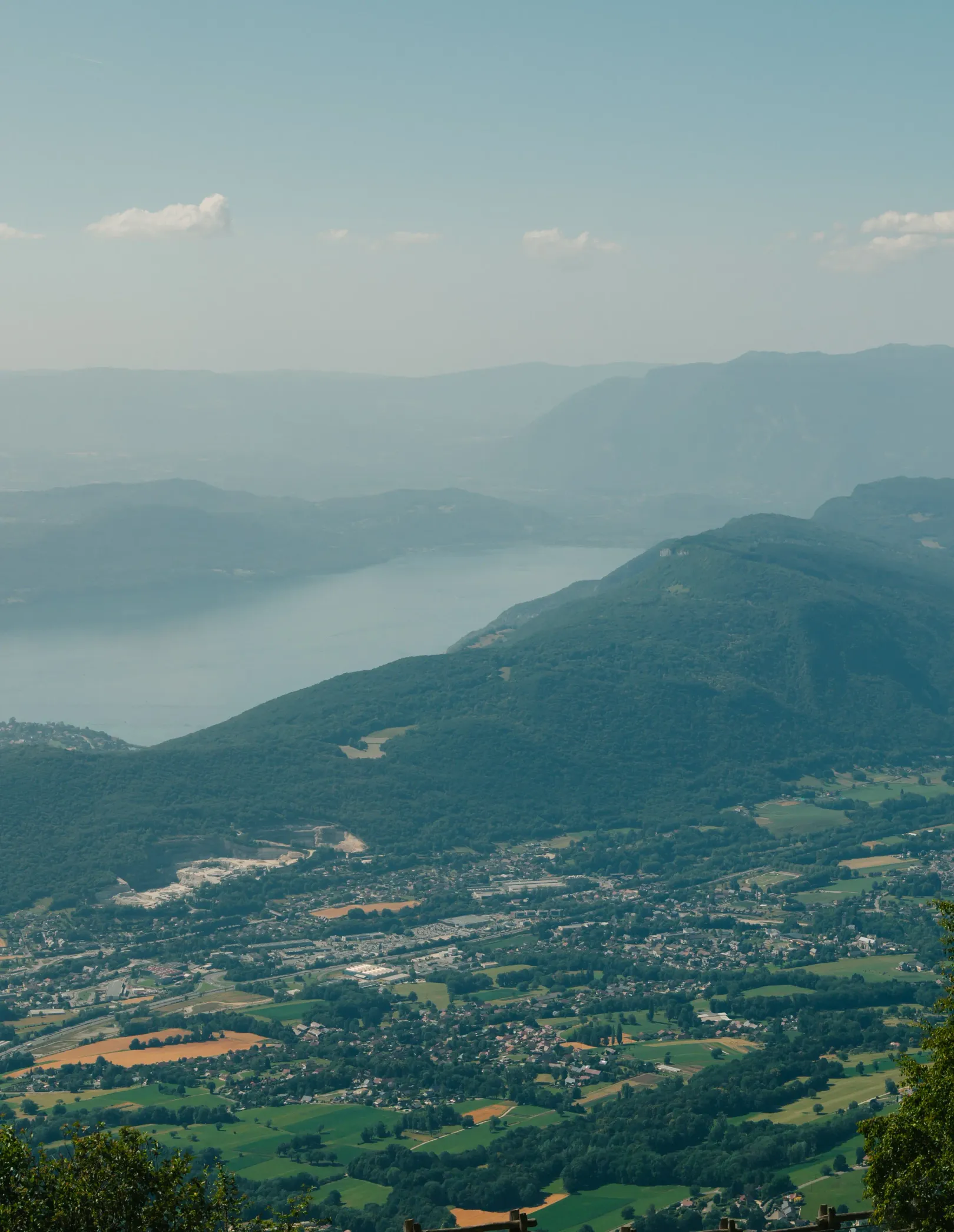 Dorf, umgeben von grünen Hügeln mit einem See im Hintergrund unter einem leicht bewölkten Himmel