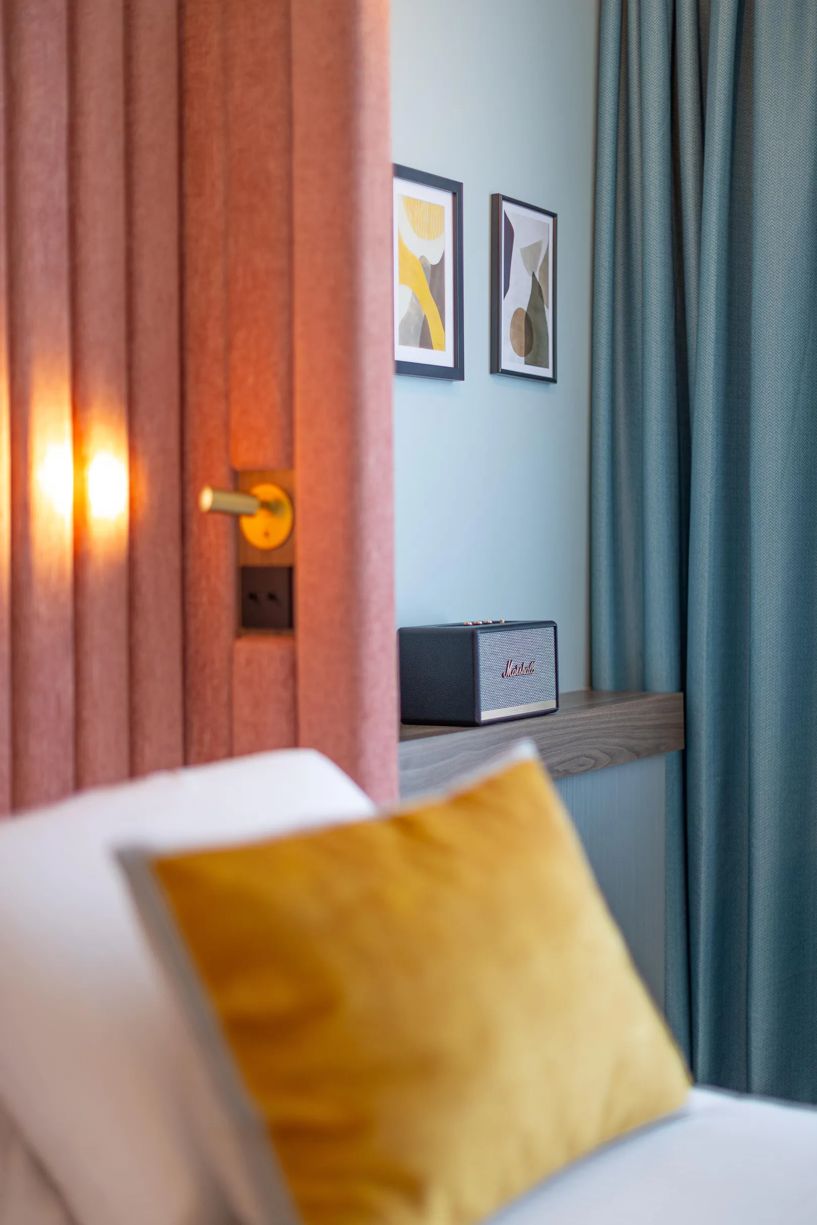 Un canapé avec un coussin jaune devant une porte en bois et un mur bleu avec deux cadres et une enceinte