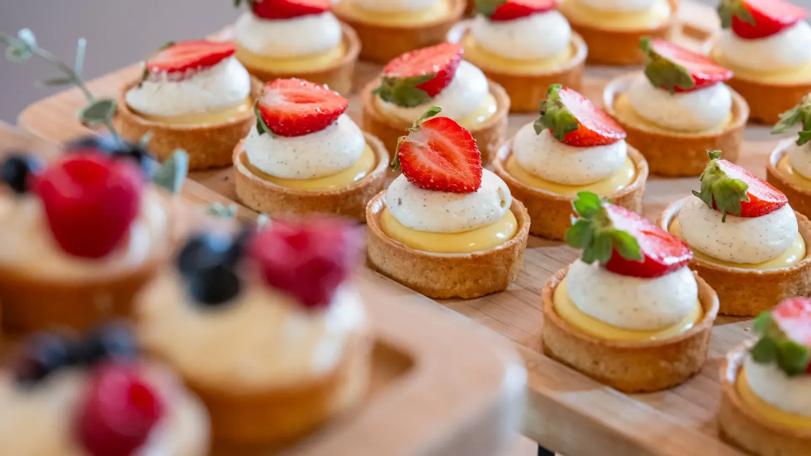 Round small cakes topped with cream and strawberries on a wooden board