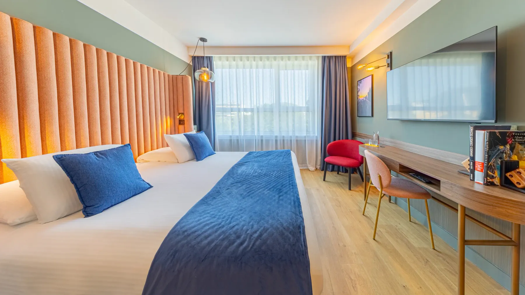 Chambre d'hôtel avec deux lits simples, un coin salon avec une table et deux chaises, une télévision à écran plat et une grande fenêtre avec des rideaux