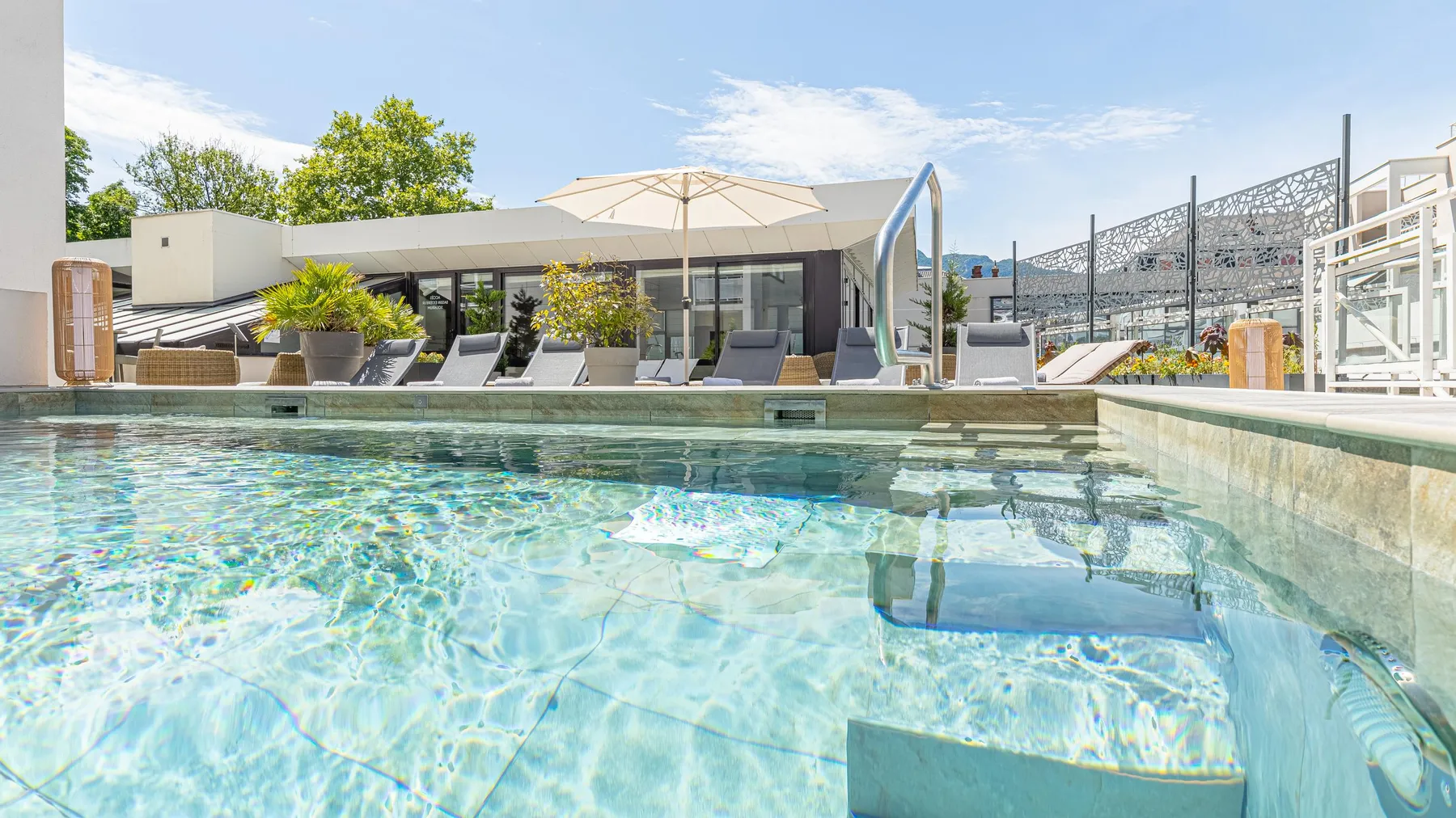 Piscine avec une vue sur une terrasse aménagée de chaises longues, de parasols et de végétation