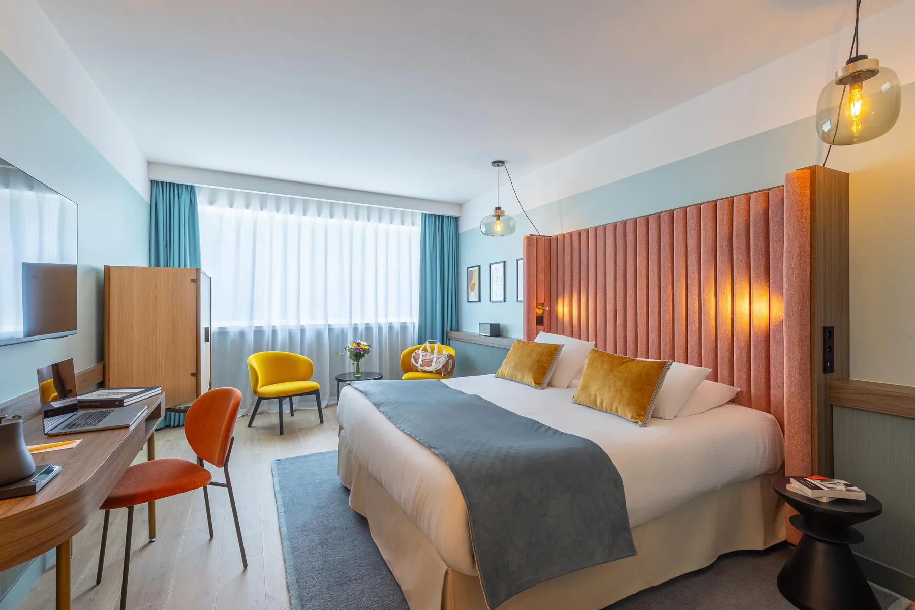 Chambre d'hôtel avec un lit double, un bureau, deux chaises, une table de chevet et des rideaux orange