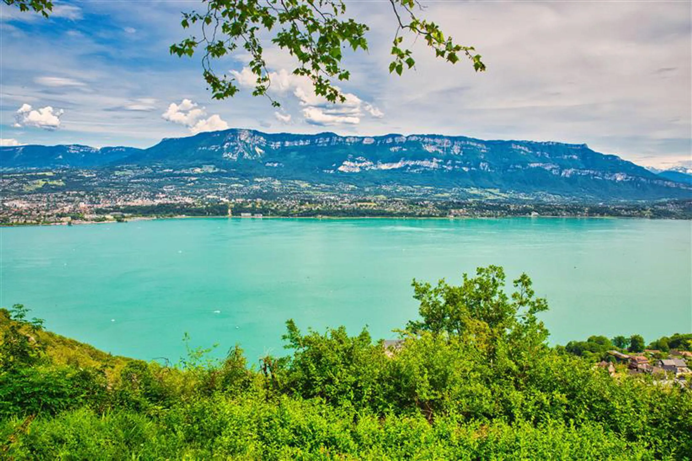 Vue d'un lac entouré de montagnes et de végétation, avec des habitations au premier plan