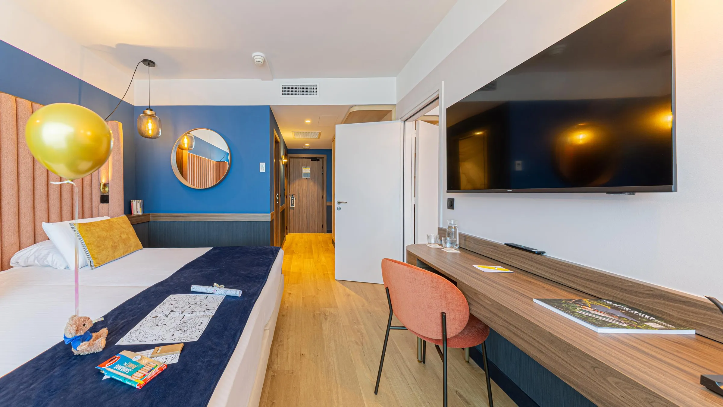 Chambre d'hôtel avec un lit, une table de travail, un téléviseur et une décoration incluant un ballon doré et un ours en peluche
