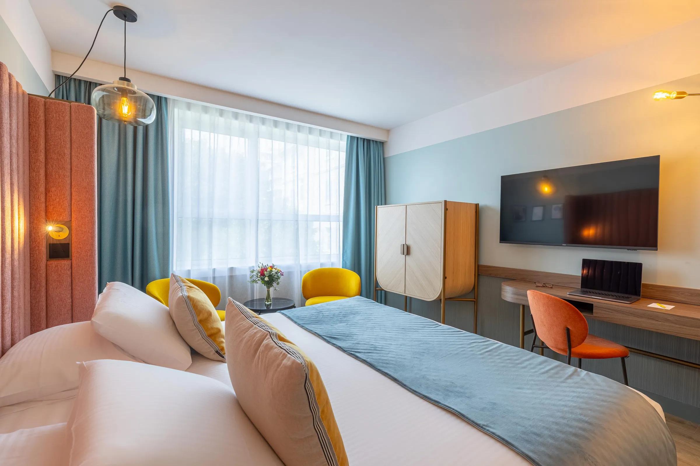 Chambre d'hôtel avec un lit double, une télévision, un bureau et une grande fenêtre avec des rideaux
