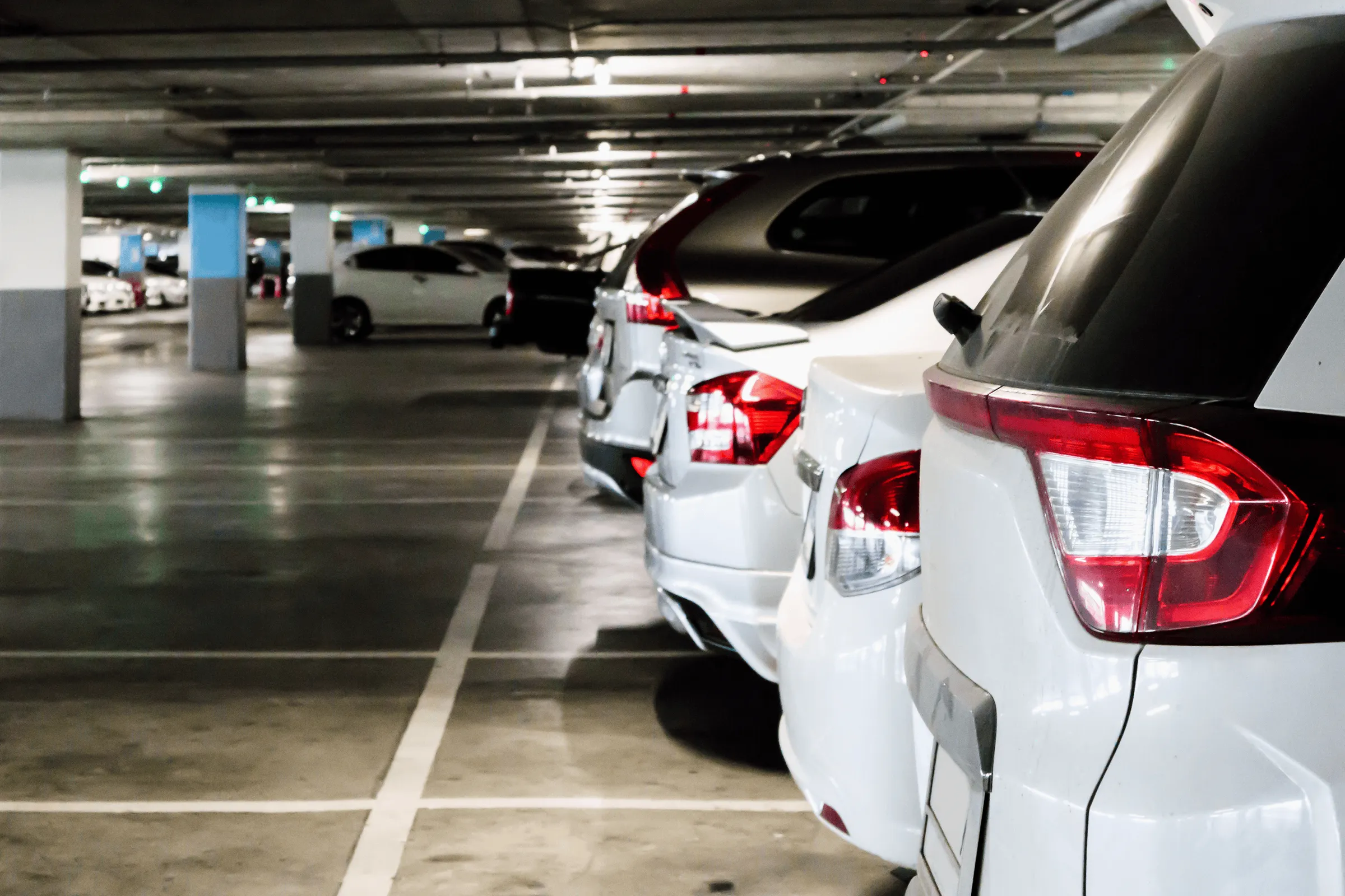Plusieurs voitures blanches garées en file dans un parking souterrain éclairé