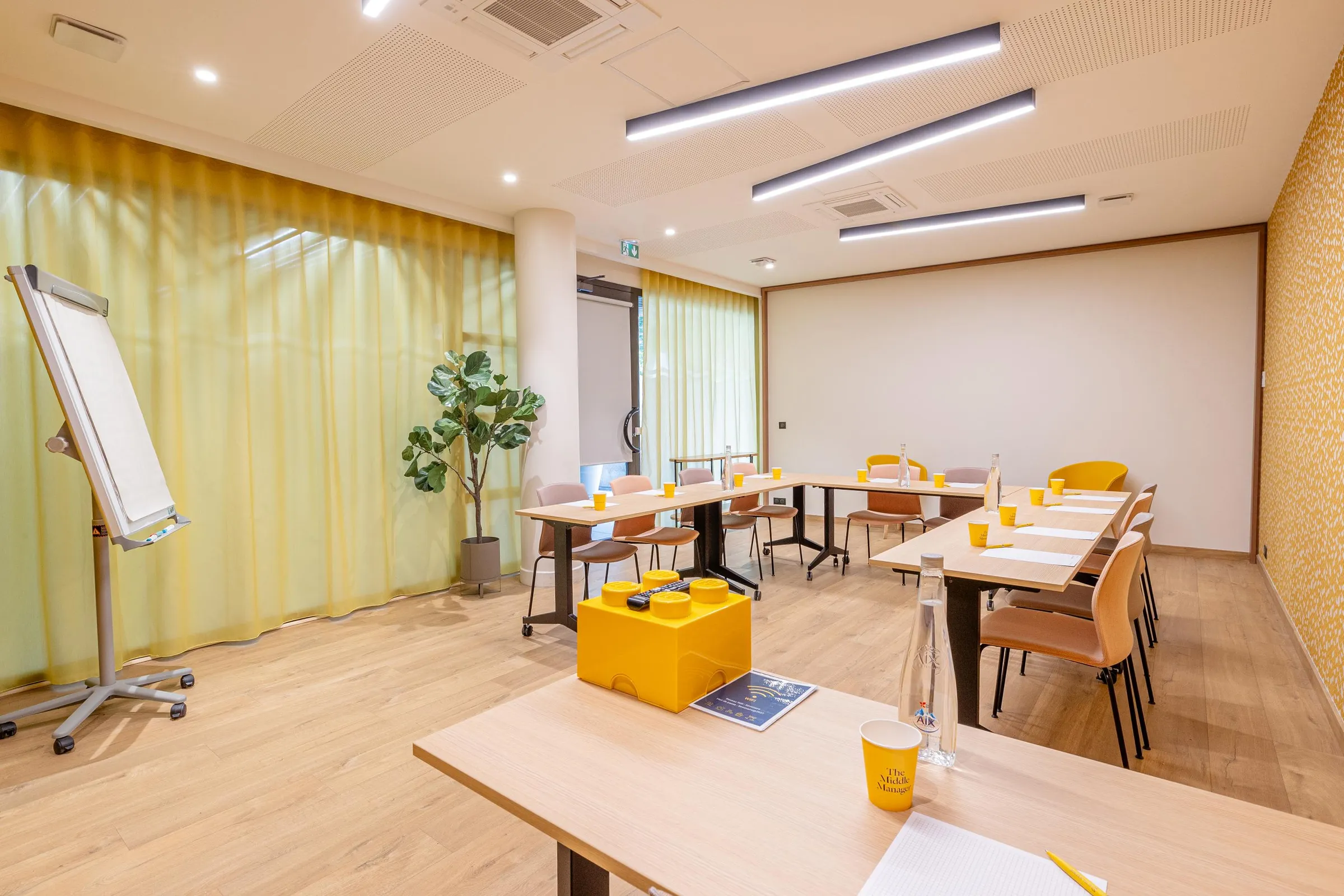 Salle de réunion avec tables, chaises, un tableau blanc, des plantes et des gobelets sur les tables