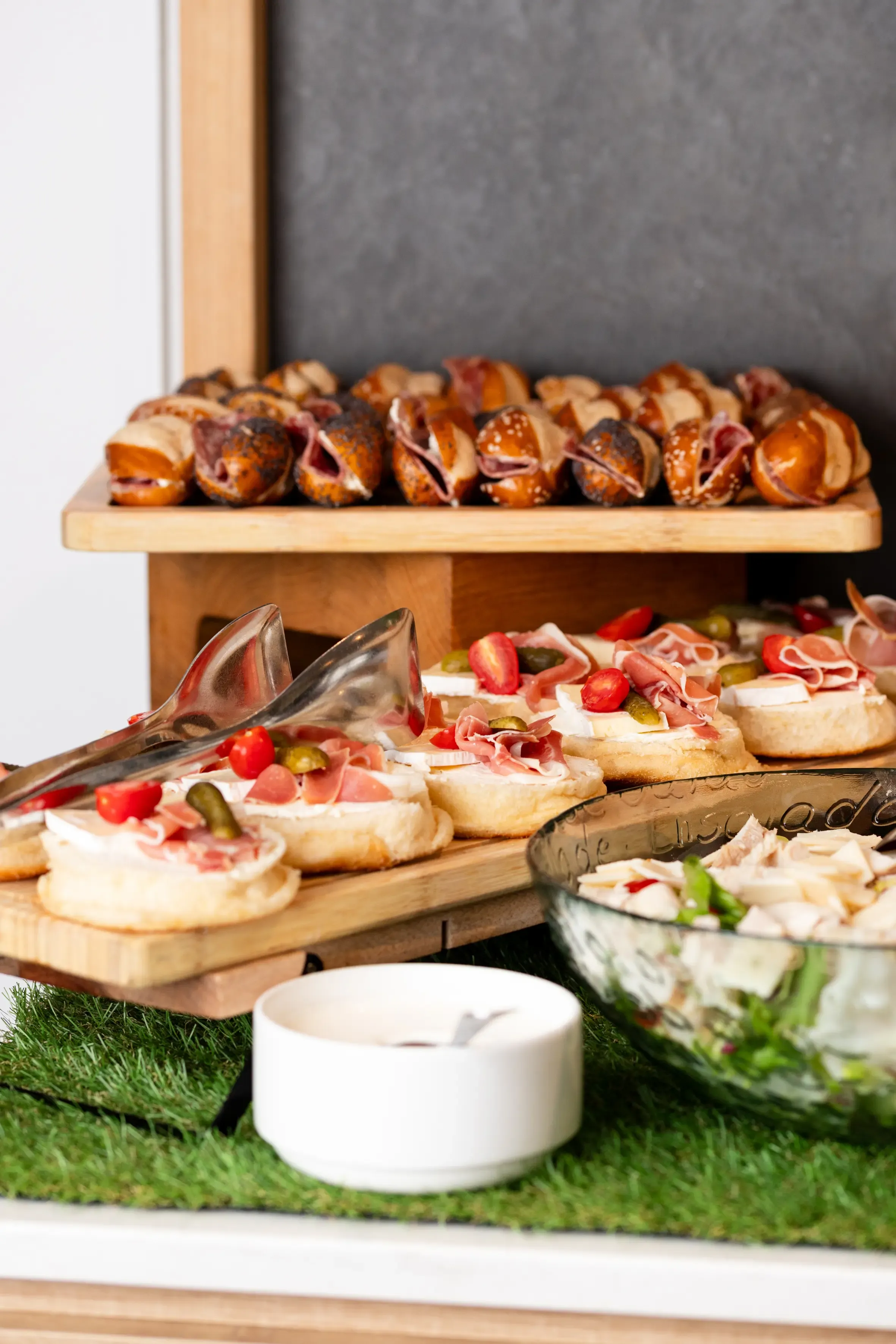 Un plateau de nourriture avec des mini-sandwiches, des canapés garnis et une salade, présenté sur une table recouverte de gazon artificiel