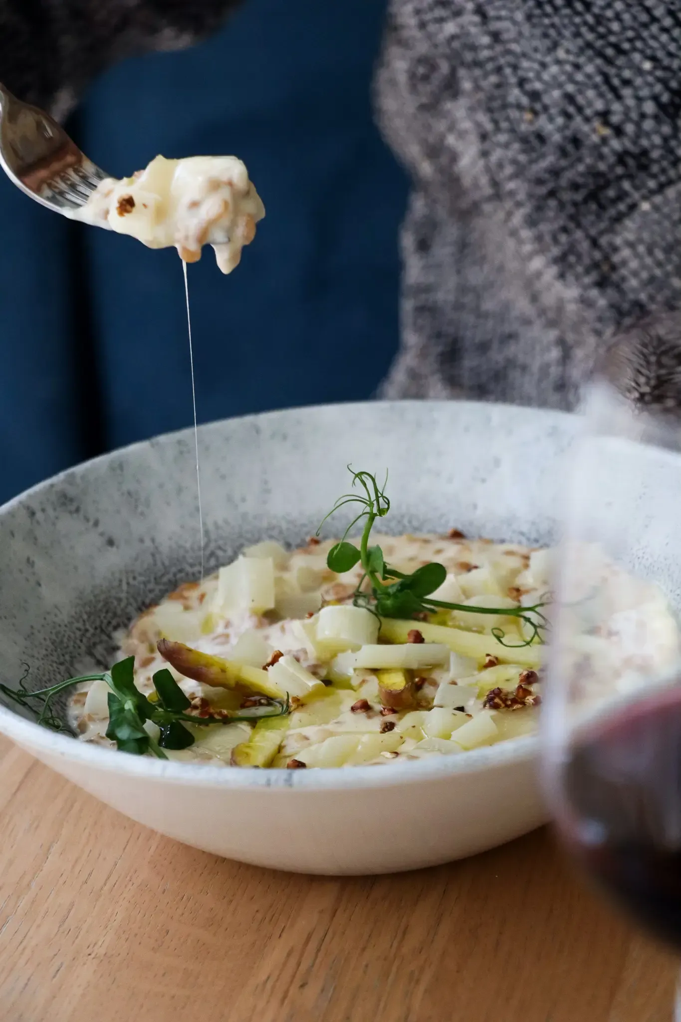 A person holds a fork with a mouthful of potato gratin topped with microgreens.