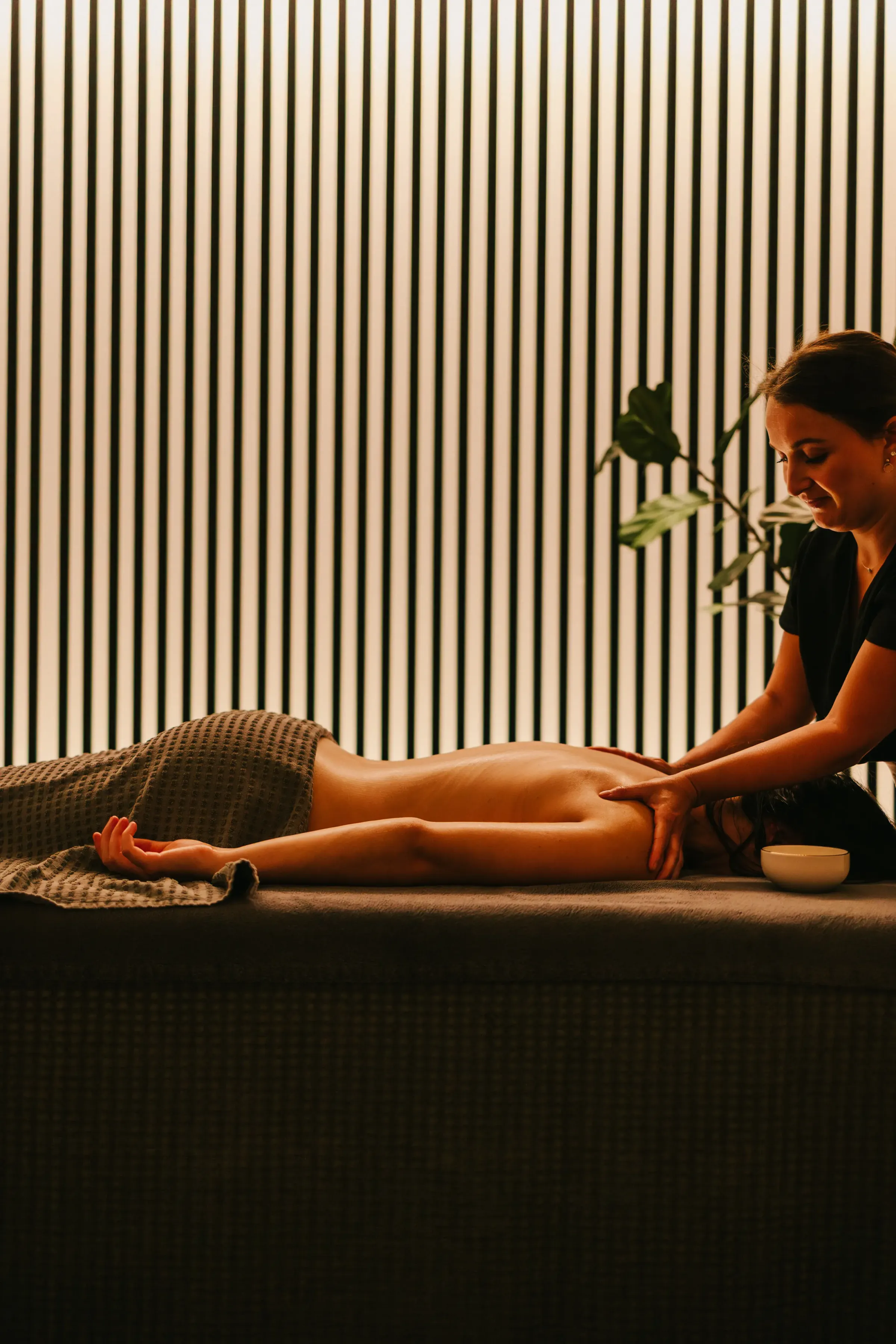A person receives a massage on a table in a room with vertically striped walls.
