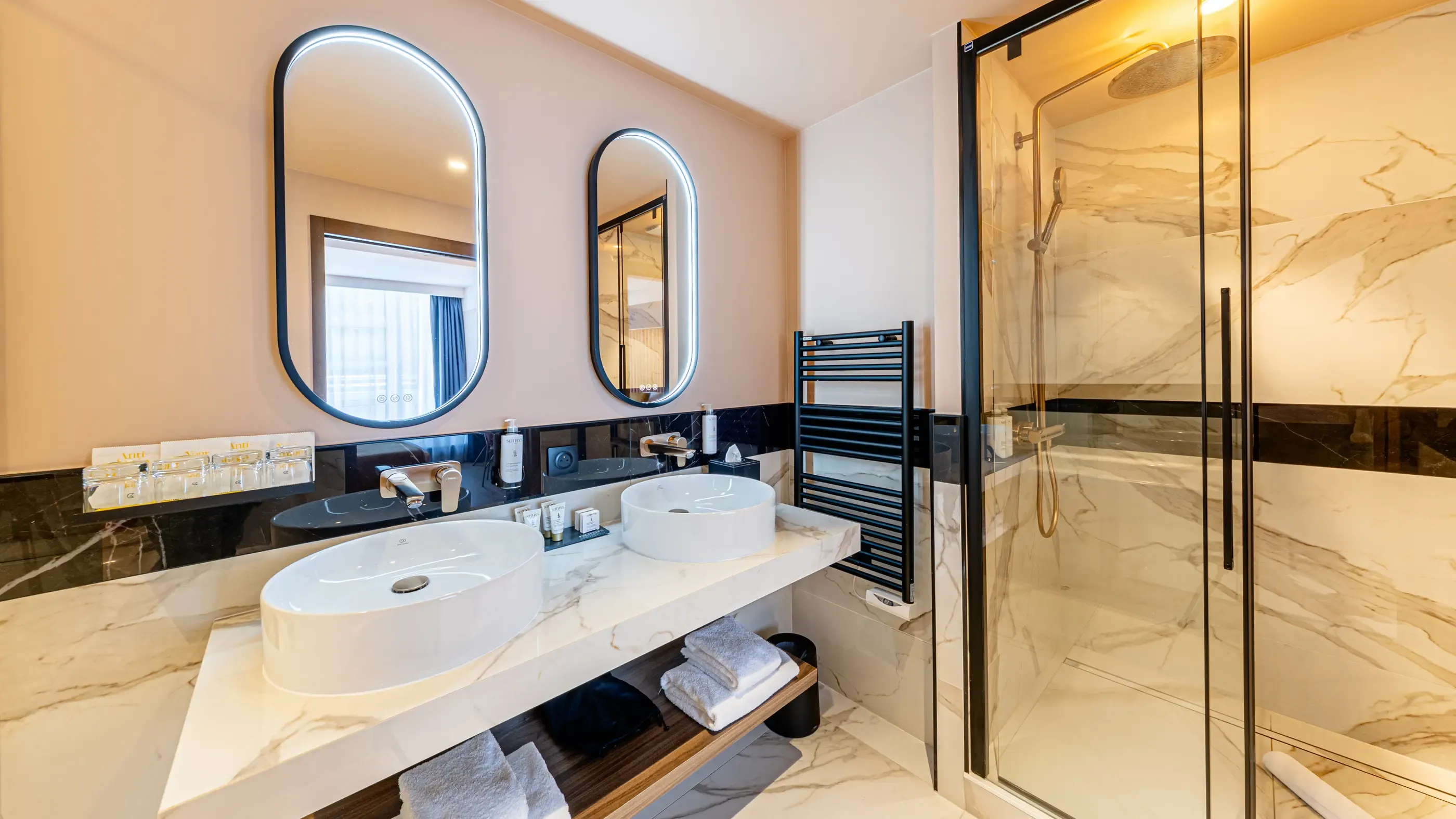 Salle de bain moderne avec double vasque, miroir ovale, douche en marbre et serviettes sur un banc