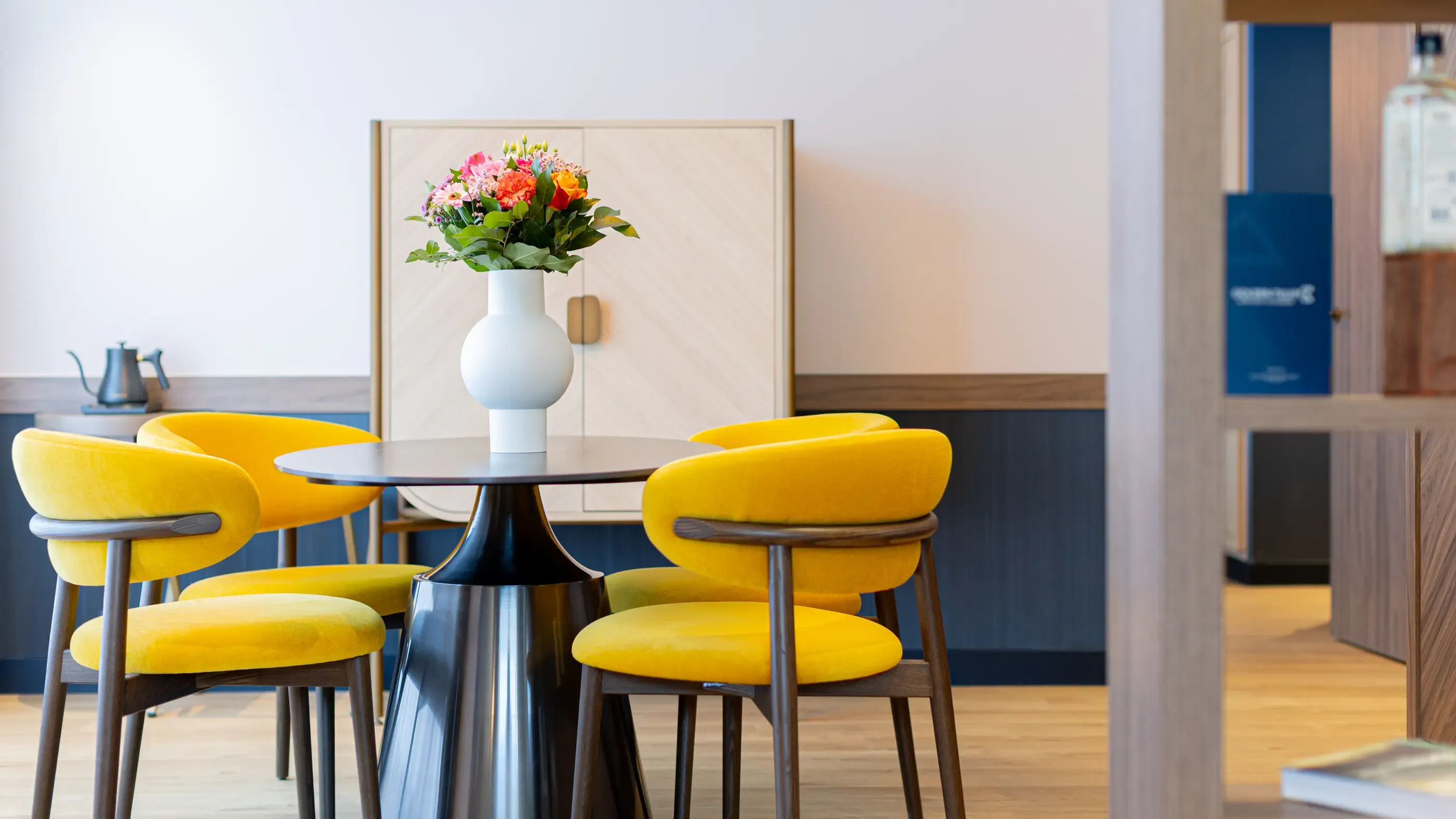 Table ronde avec quatre chaises jaunes et un vase de fleurs au centre dans une pièce moderne