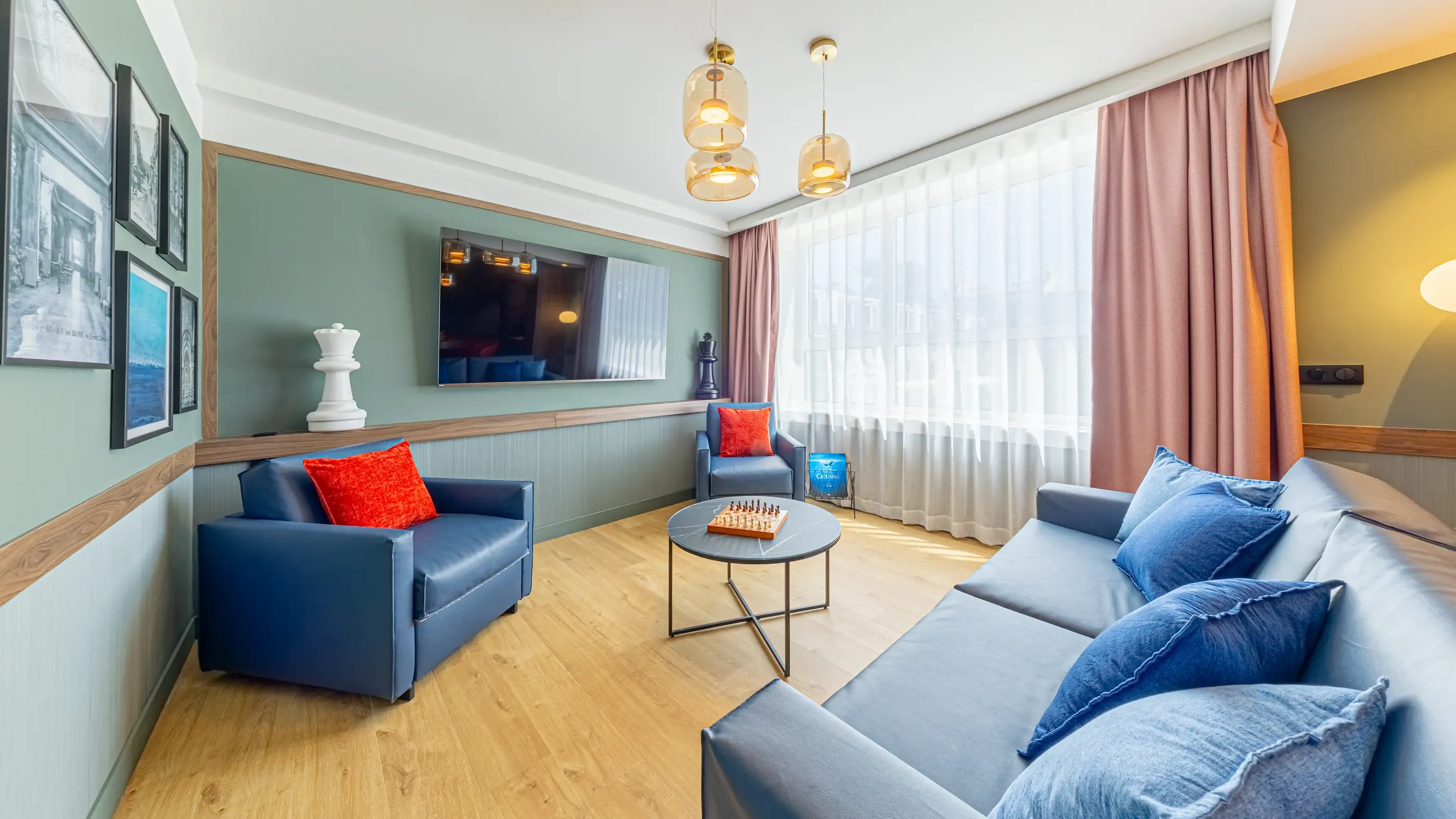 Living room with gray sofa, blue armchair, coffee table, and chessboard, lit by pendant lights