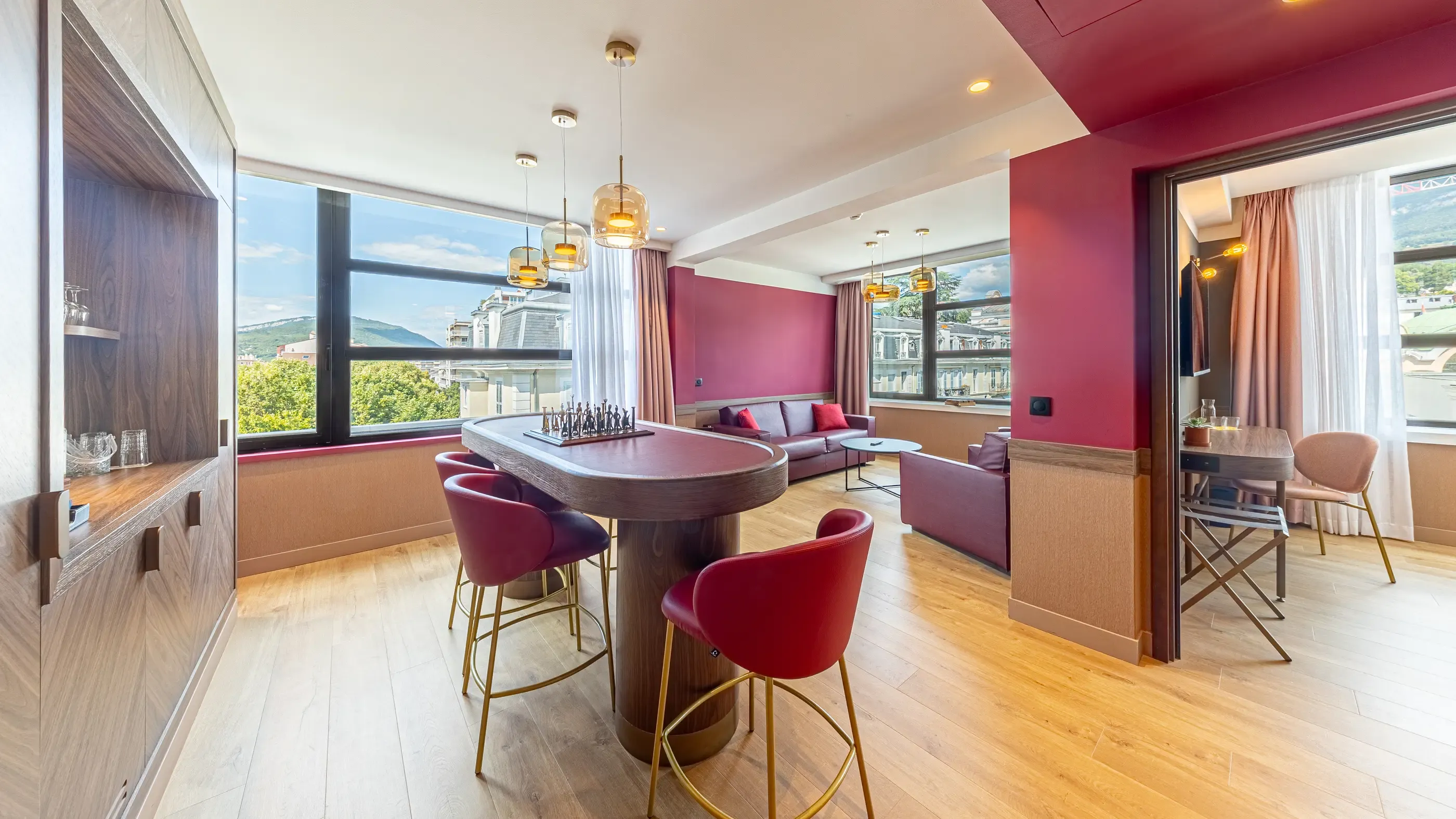 Moderner Salon mit ovalem Tisch, roten Stühlen, grauem Sofa und Panoramablick auf eine Stadt