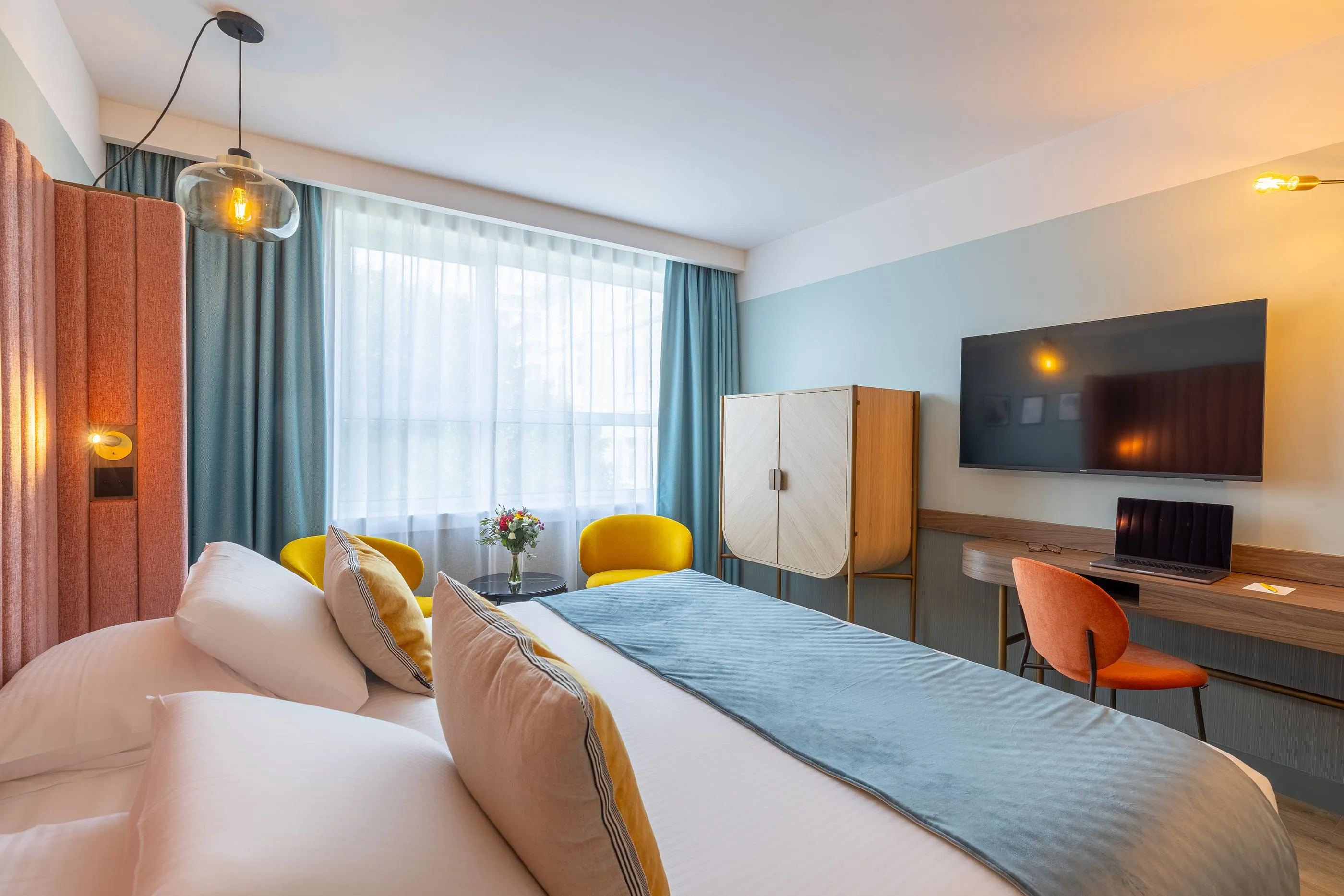 Chambre d'hôtel avec un lit double, une télévision, un bureau et une grande fenêtre avec des rideaux