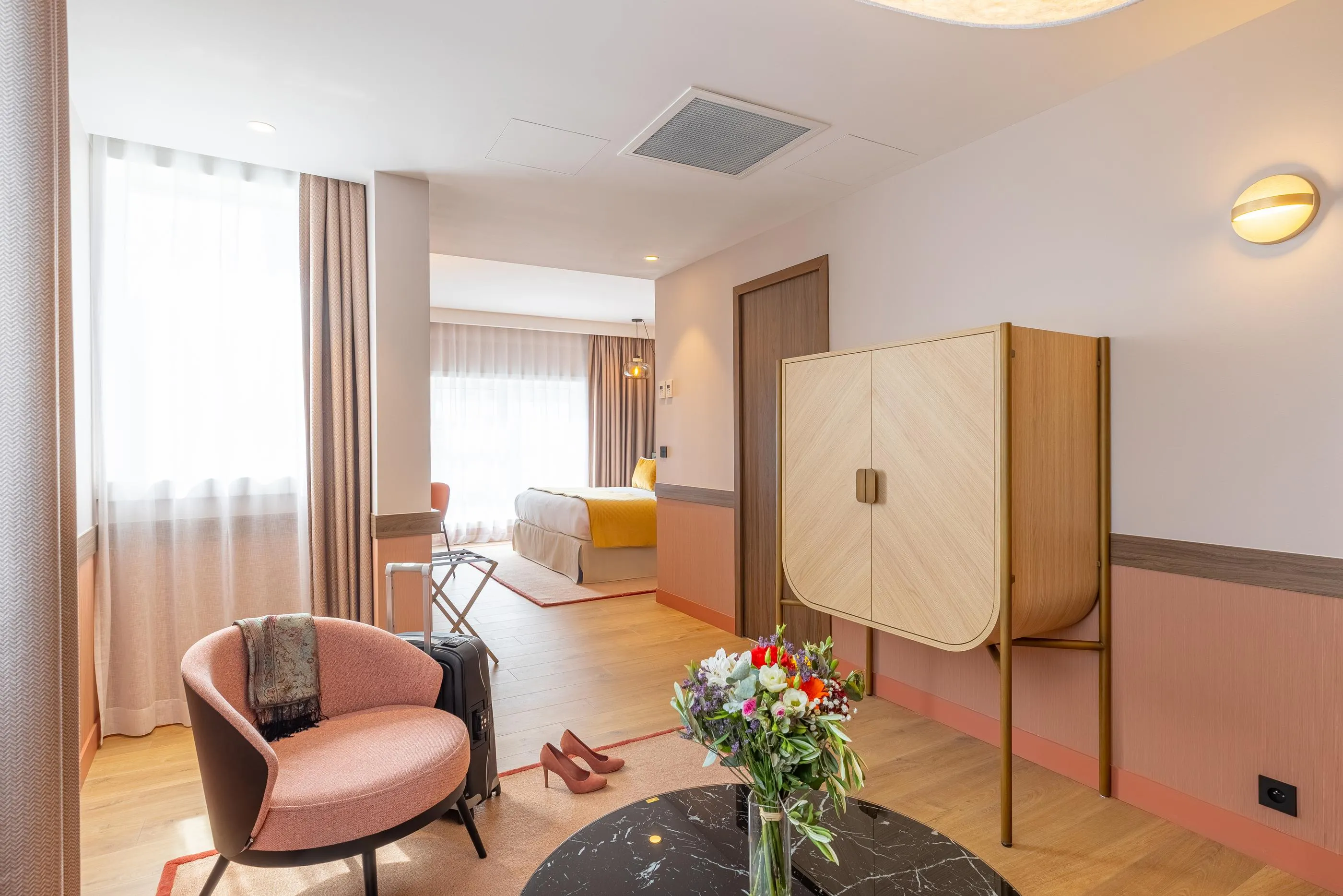 Chambre d'hôtel avec un fauteuil, une table basse, un vase de fleurs, un lit et une armoire visible