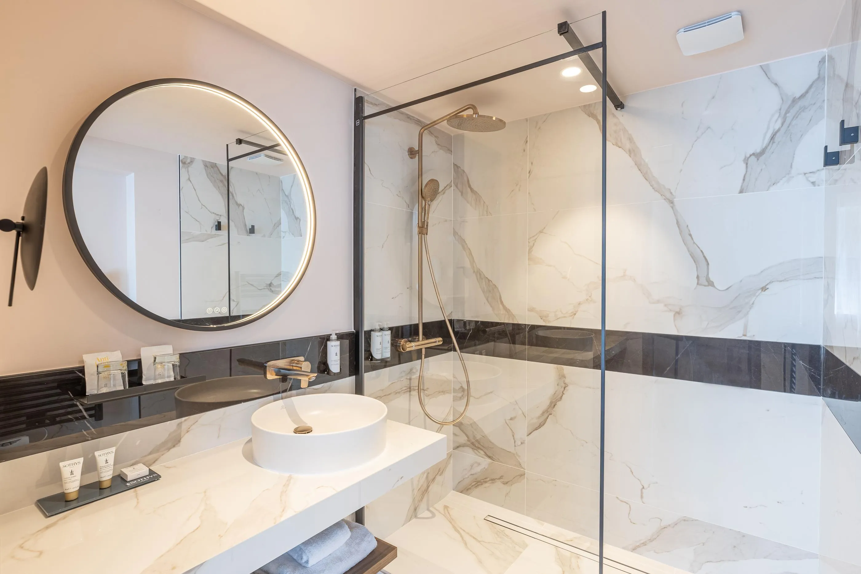 Moderne Badezimmer mit Waschbecken, rundem Spiegel und Regendusche hinter einer Glaswand