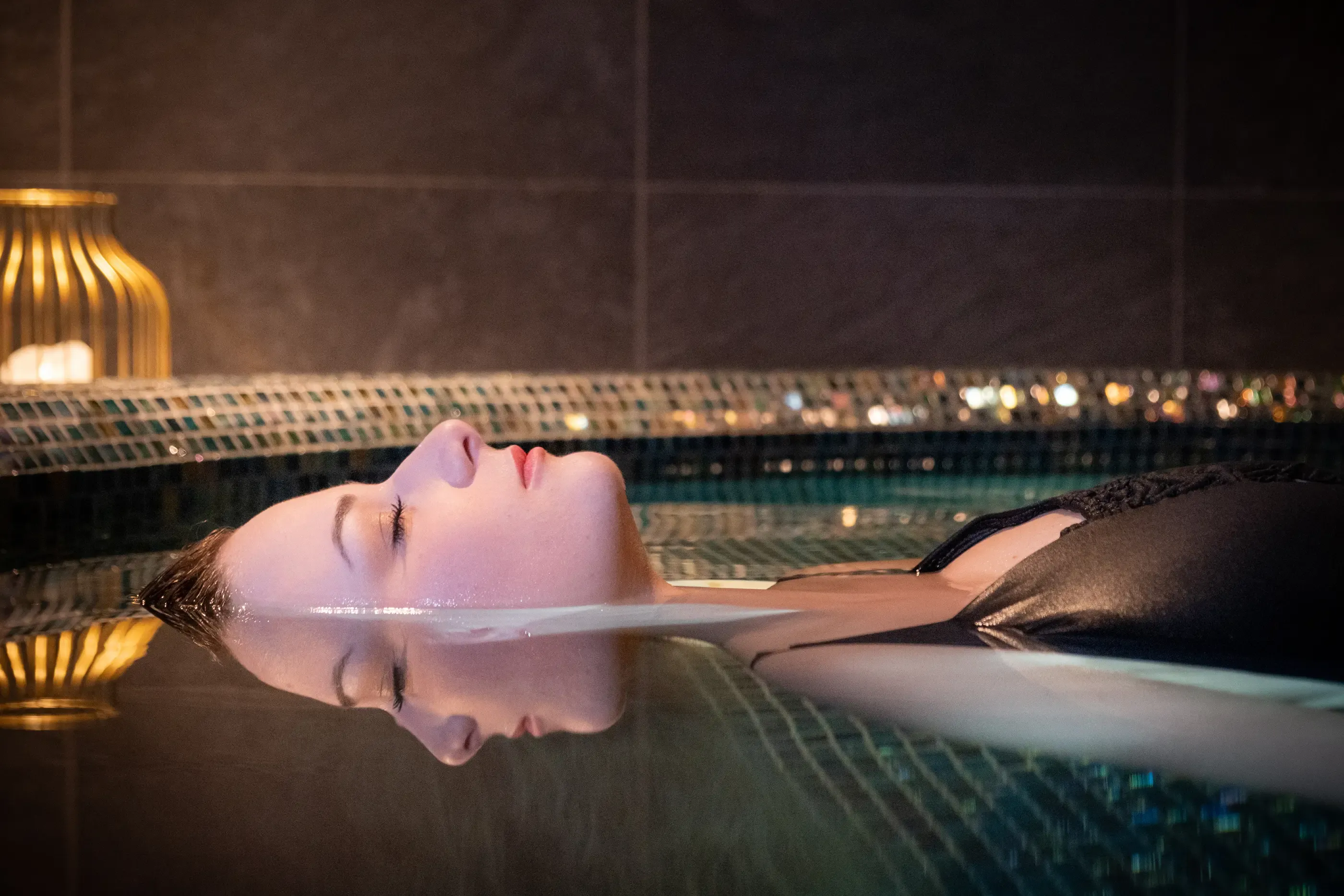 A person lying on their back in a pool with a blurred night view in the background