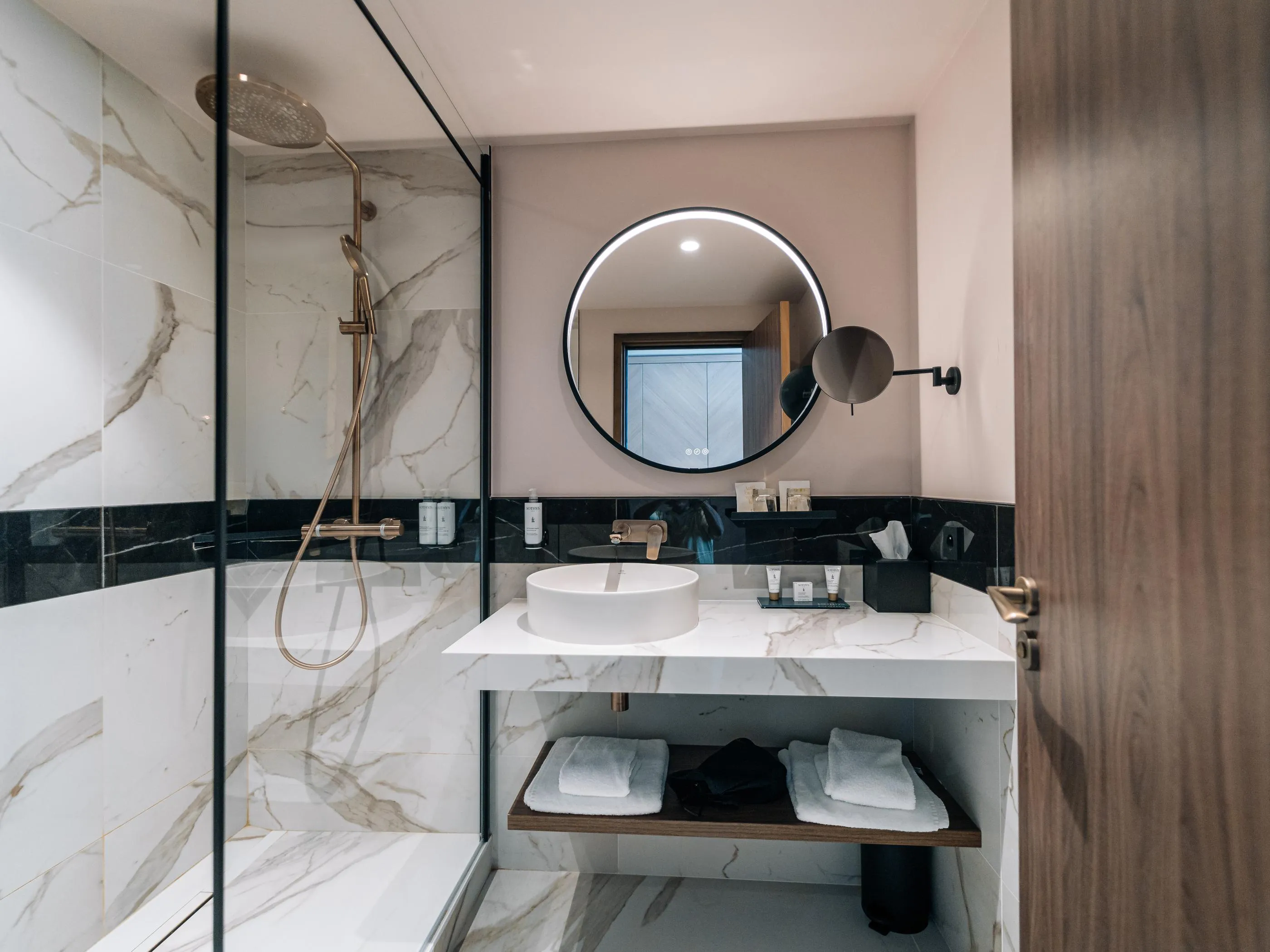 Modern bathroom with marble shower, white sink, and illuminated round mirror