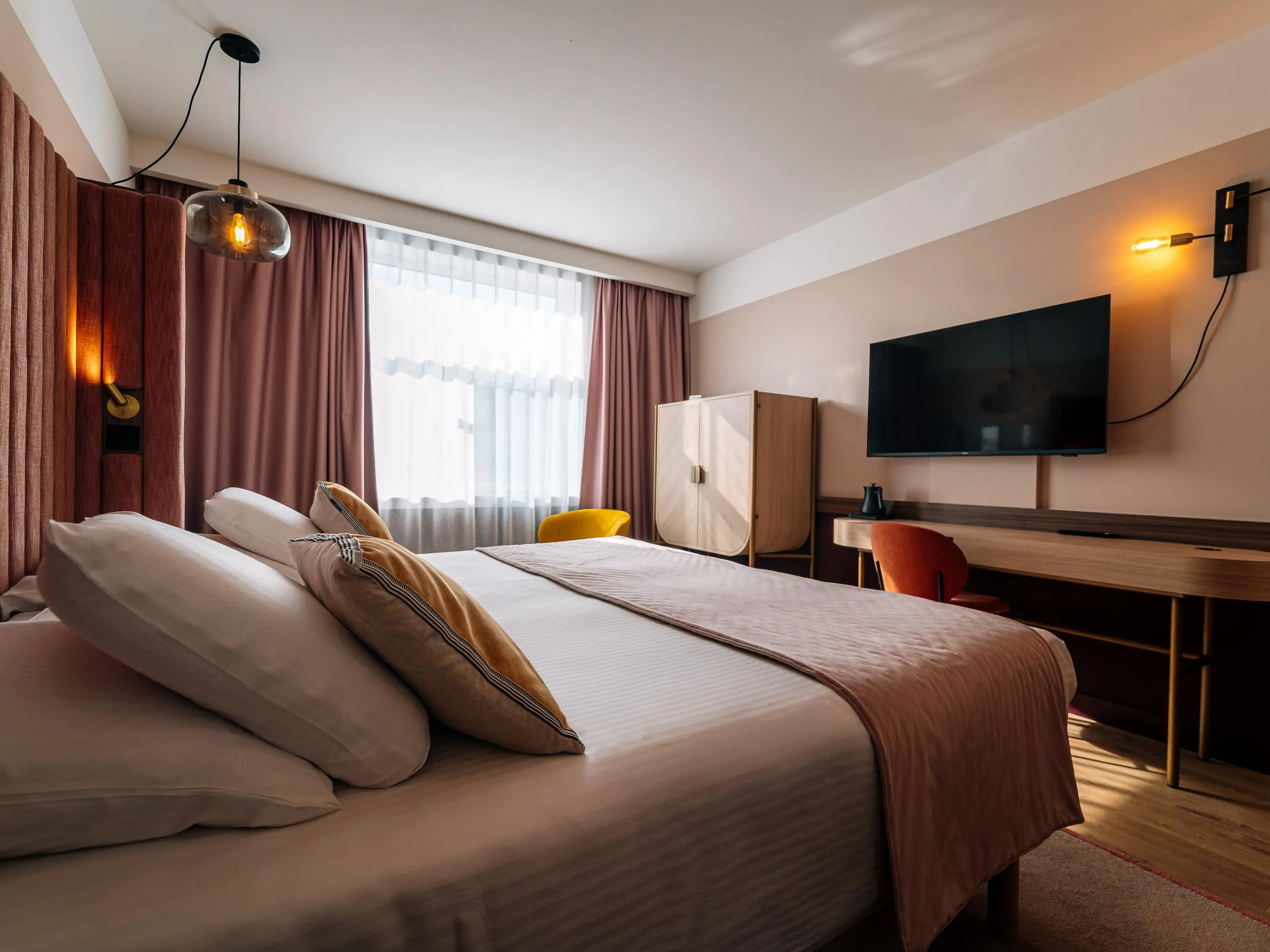Hotelzimmer mit einem Doppelbett, einem Flachbildfernseher, einem Schreibtisch und braunen Vorhängen