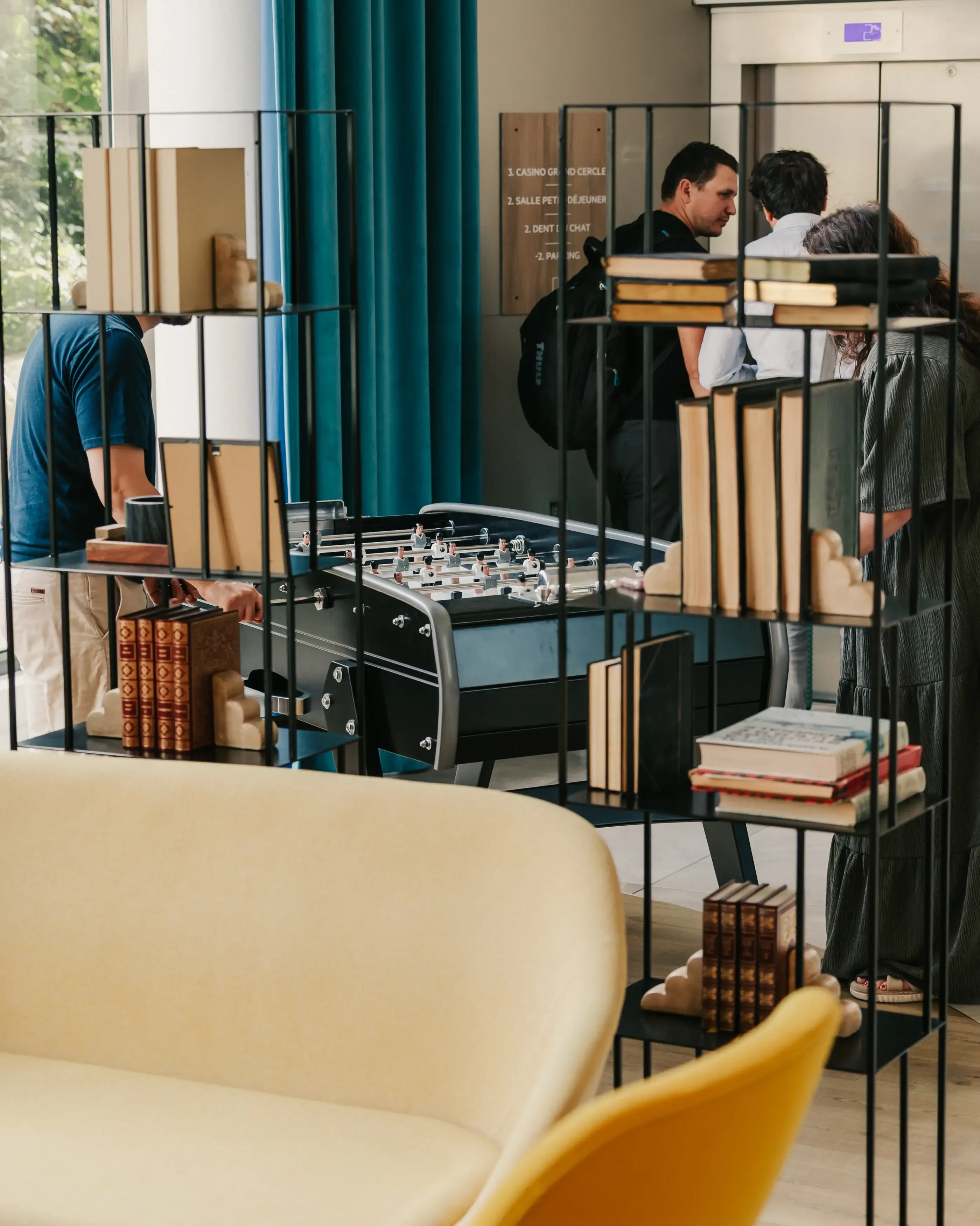 People are playing foosball in an indoor space with shelves filled with books and sofas.