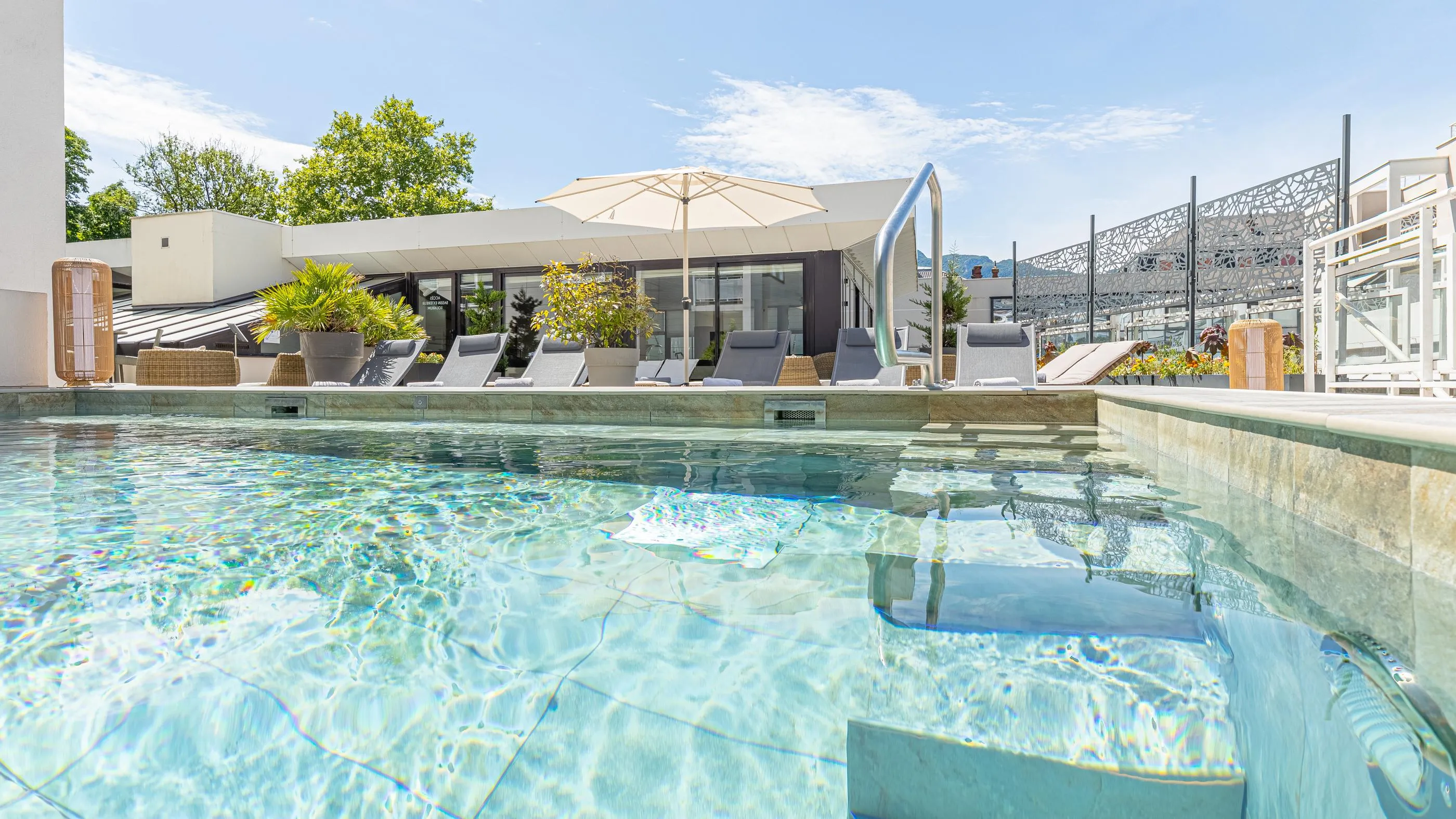Piscine avec une vue sur une terrasse aménagée de chaises longues, de parasols et de végétation