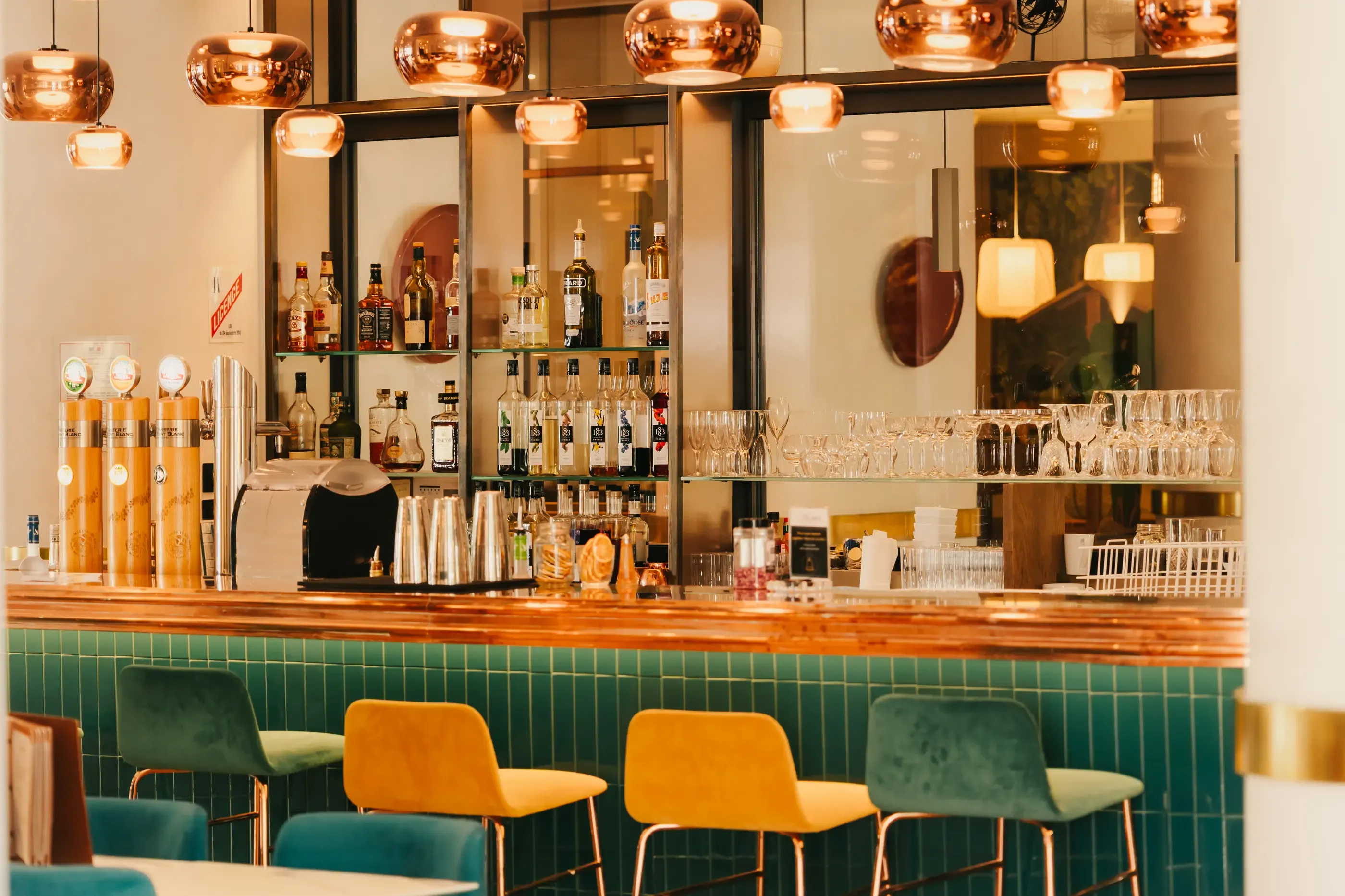 A bar with shelves filled with bottles of alcohol, glasses, and colorful stools in front of a counter.