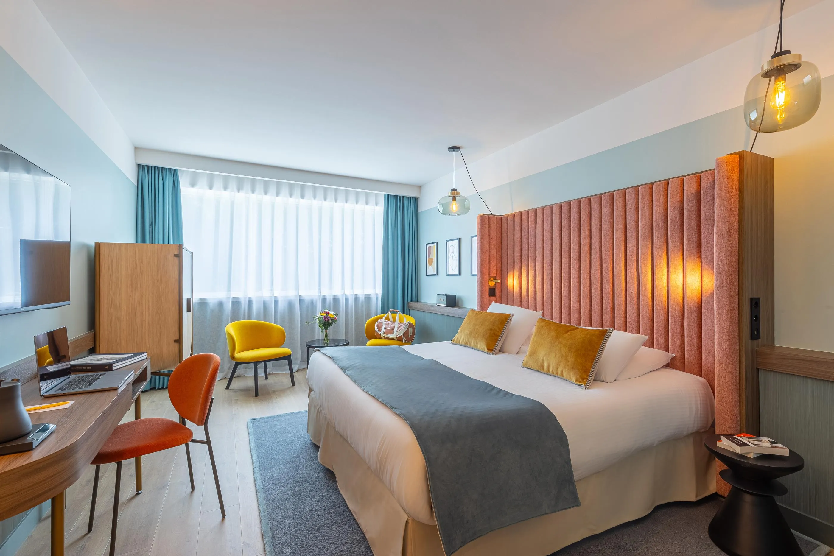 Chambre d'hôtel avec un lit double, un bureau, deux chaises, une table de chevet et des rideaux orange