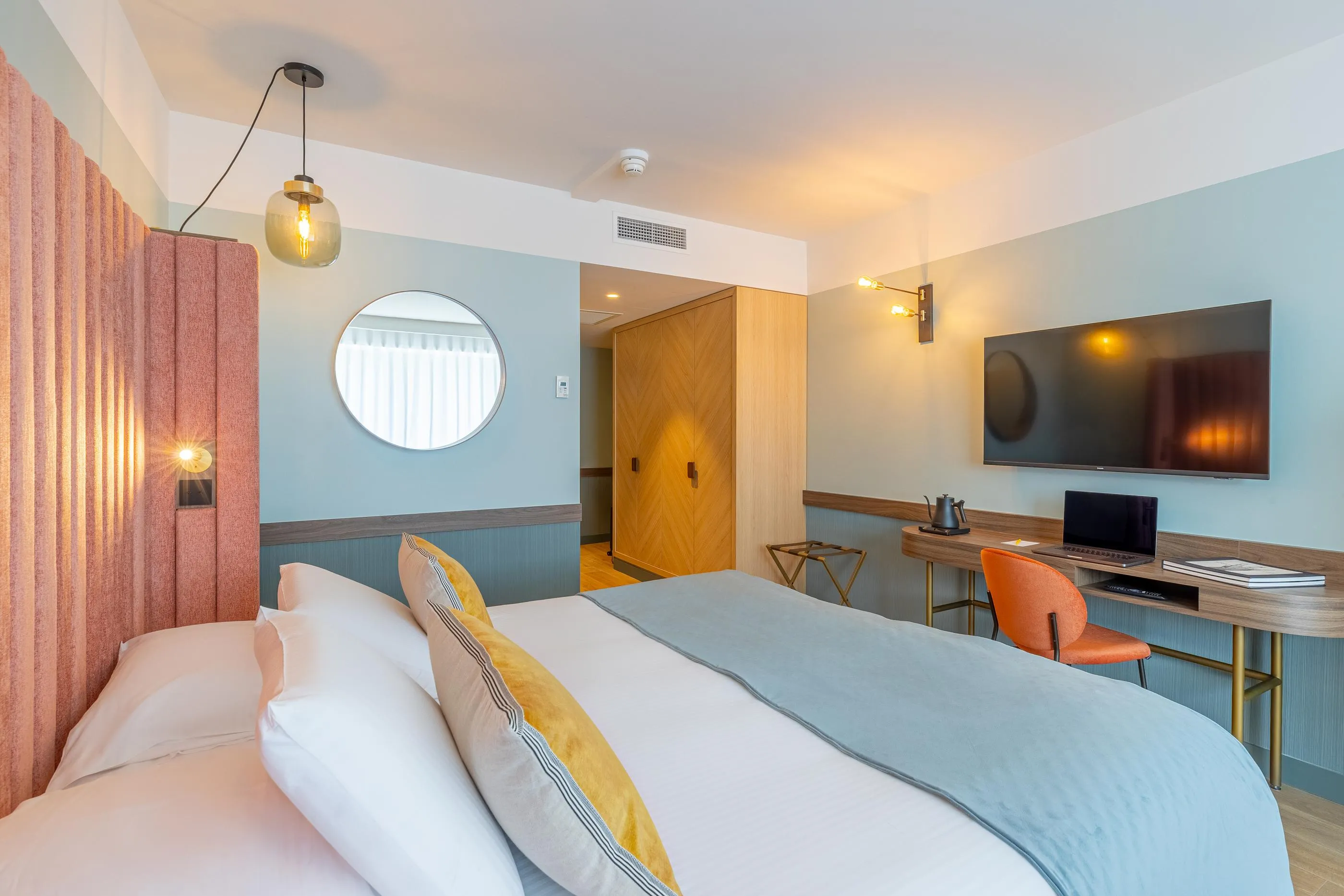 Hotelzimmer mit einem Doppelbett, einem Fernseher, einem Schreibtisch und Wandlampen