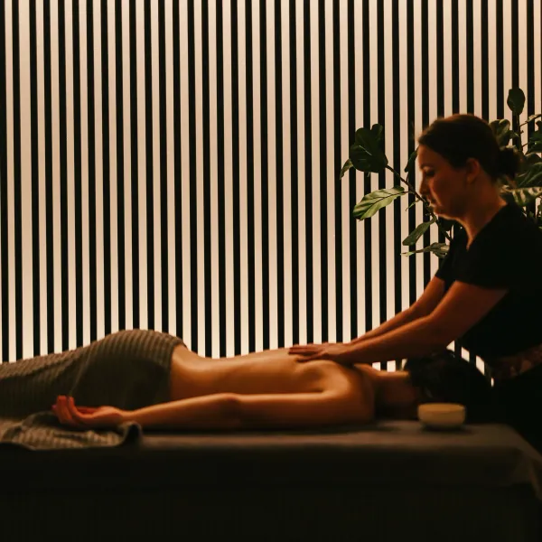 Eine Person erhält eine Massage auf einem Tisch in einem Raum mit einer Pflanze und vertikalen Jalousien.