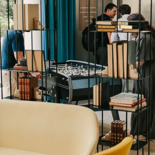 Menschen spielen an einem Kickertisch in einem Innenraum mit Bücherregalen und Sofas.