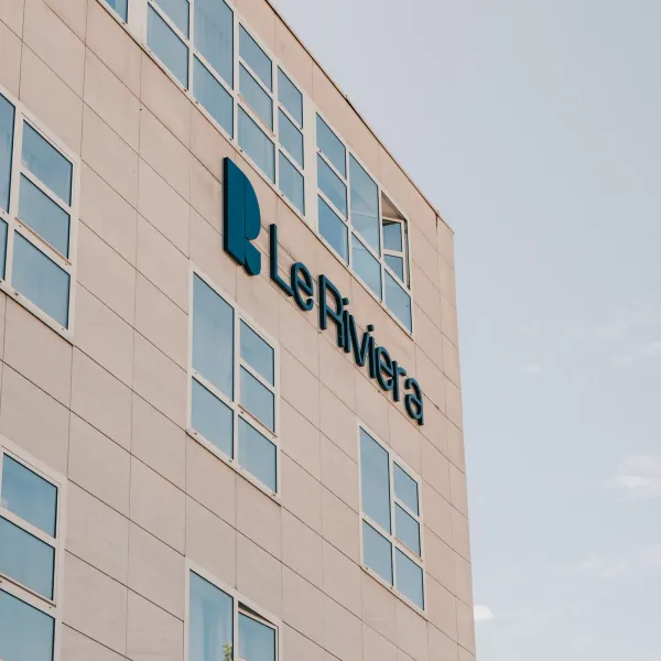 Beiges Gebäude mit rechteckigen Fenstern, das das Logo und den Namen "Le Riviera" in Blau zeigt