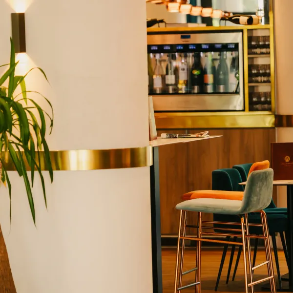 Ein Restaurantinnenraum mit Tischen, Stühlen und einer im Hintergrund sichtbaren Bar, beleuchtet durch Wandlampen
