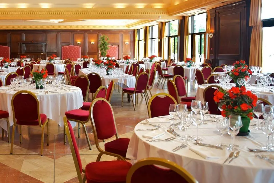 Salle de réception avec tables rondes couvertes de nappes blanches, des chaises rouges et des fleurs rouges en centre de table