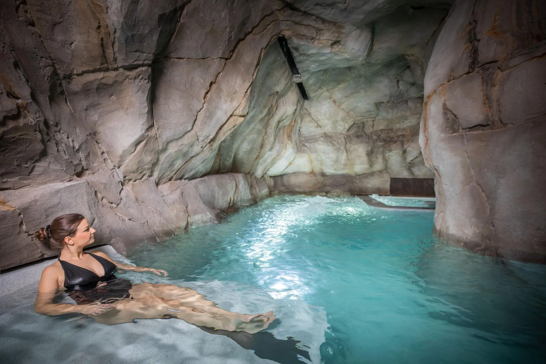 Une personne est allongée dans une piscine d'eau bleue située dans une grotte artificielle en pierre
