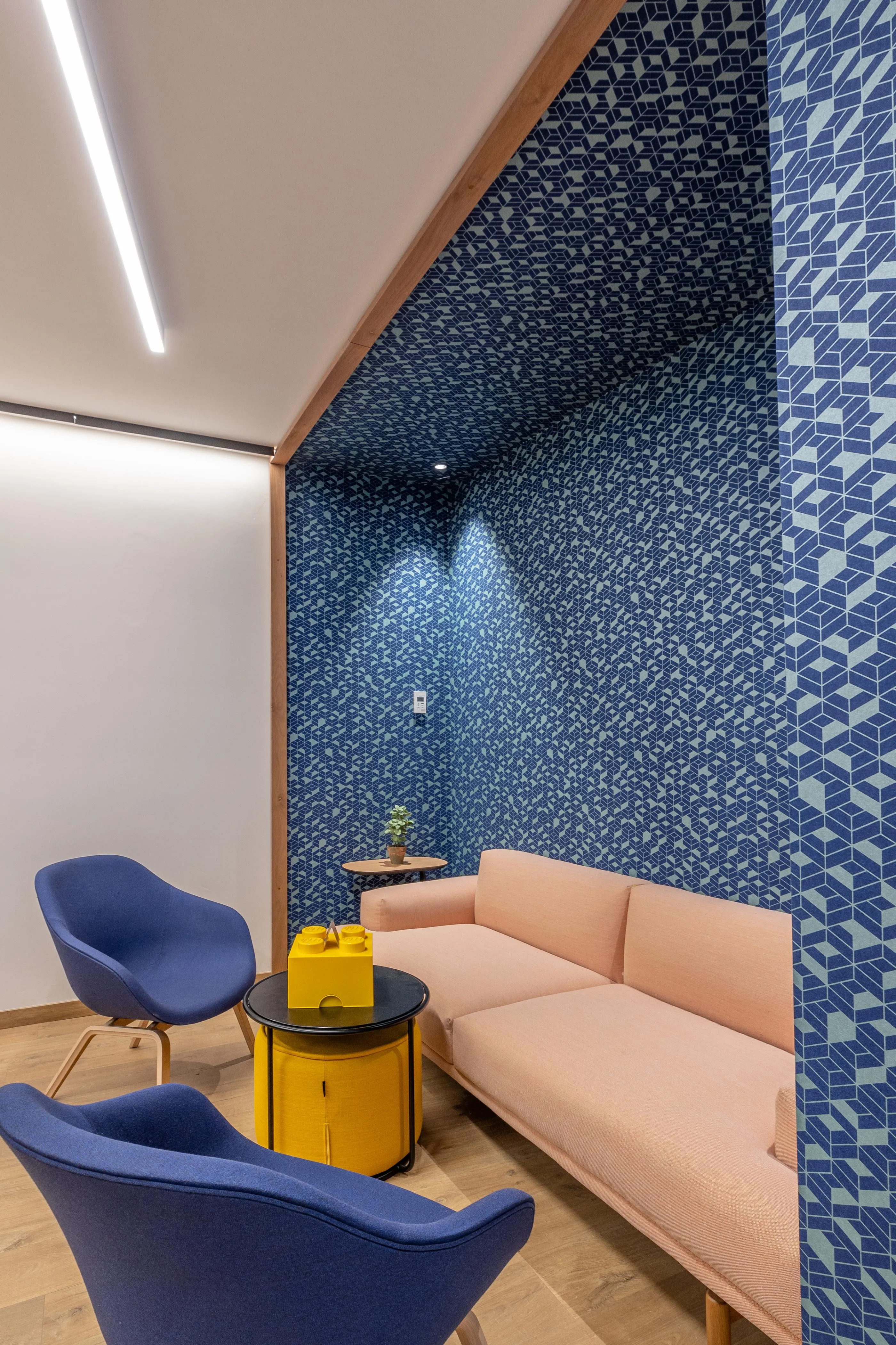 Un salon avec un canapé beige, deux fauteuils bleus et une table basse jaune, devant un mur décoré de motifs géométriques bleus et gris