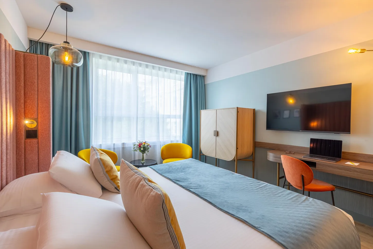 Chambre d'hôtel avec un lit double, une télévision, un bureau et une grande fenêtre avec des rideaux