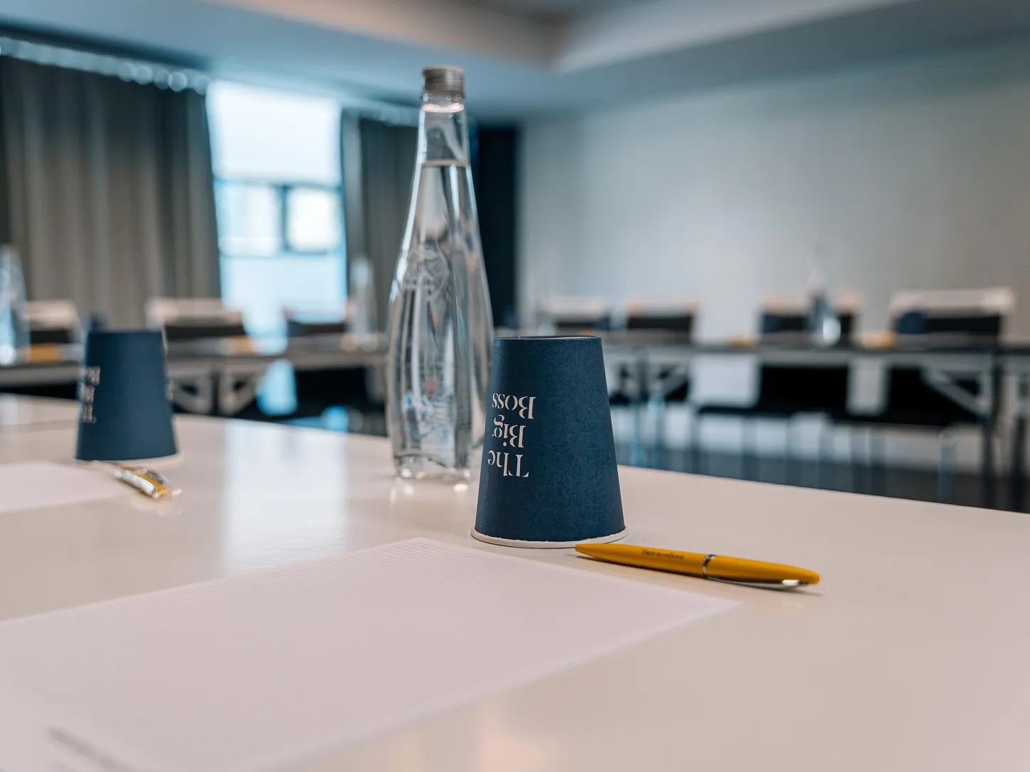 A bottle of water, a cup, and a pen on a table in a meeting room.