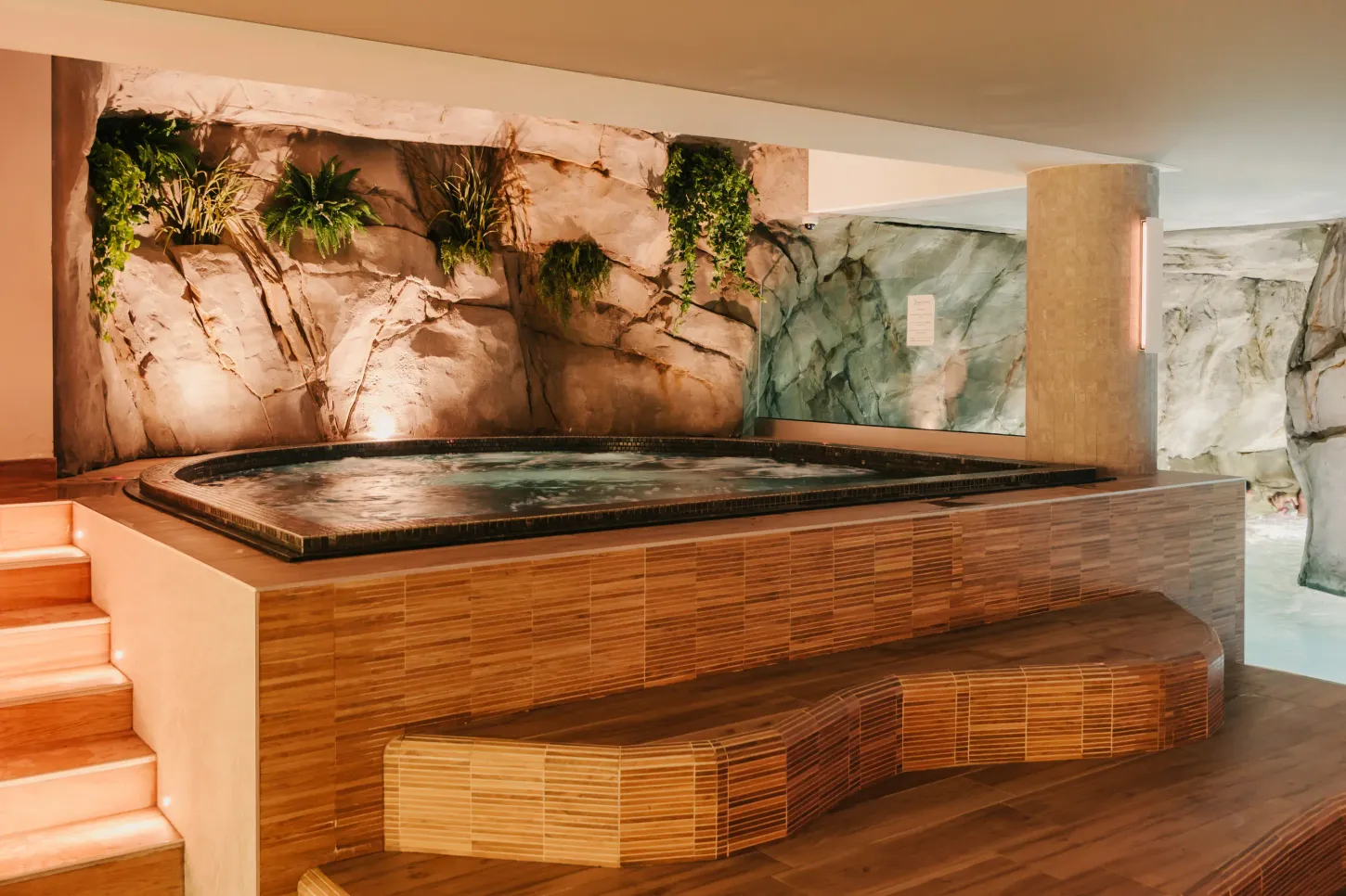 Piscine intérieure avec paroi rocheuse décorée de plantes vertes et bancs en bambou à proximité