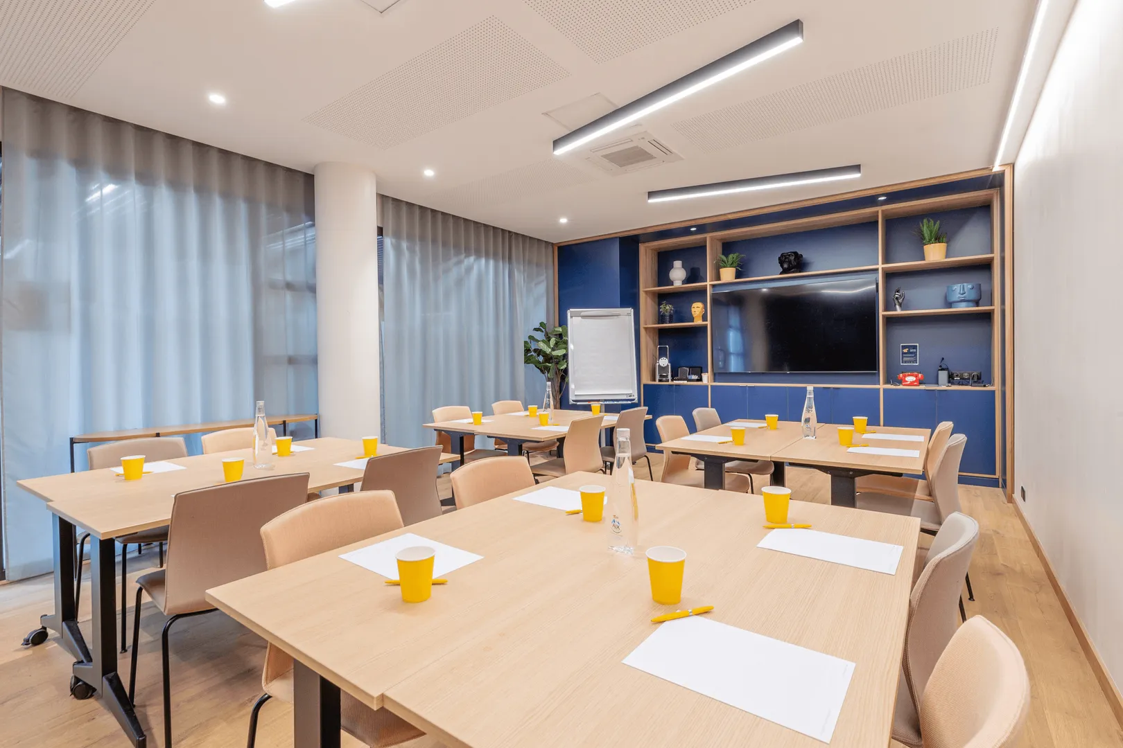 Meeting room with tables, chairs, cups, water bottles, and a screen in the background.