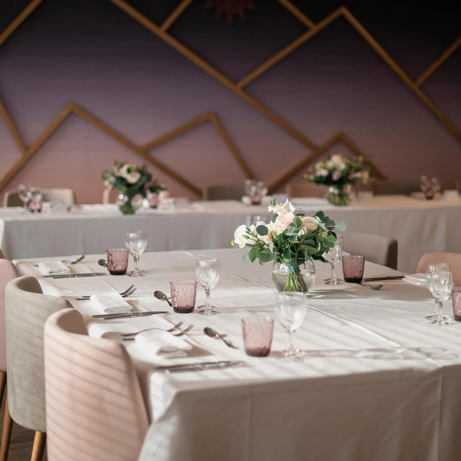 Table set with glasses, cutlery, and flowers in an indoor space with walls decorated with geometric patterns.