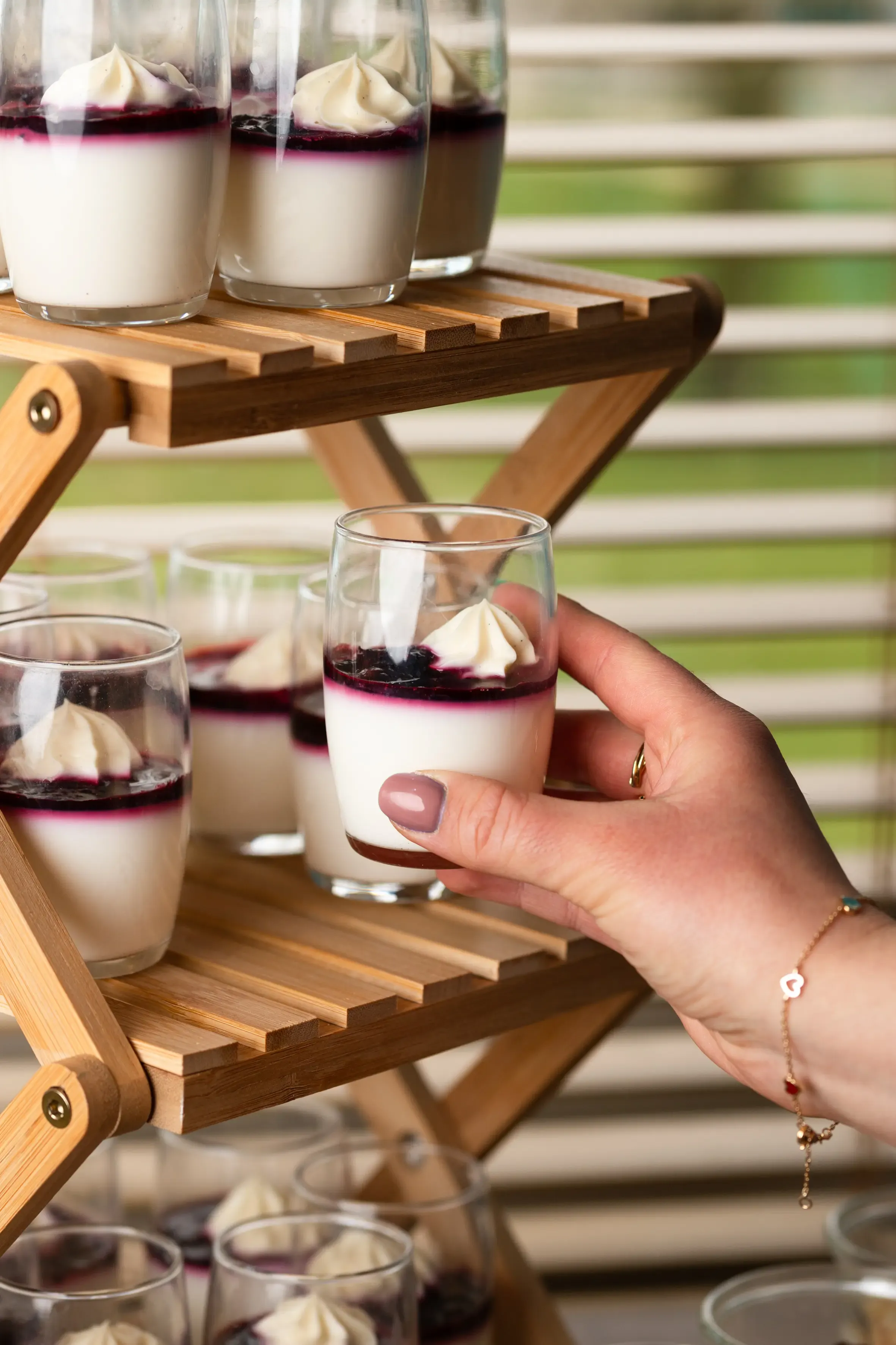 Eine Hand hält ein Dessertglas mit Vanille und Beeren auf einem Holztablett mit anderen ähnlichen Gläsern.